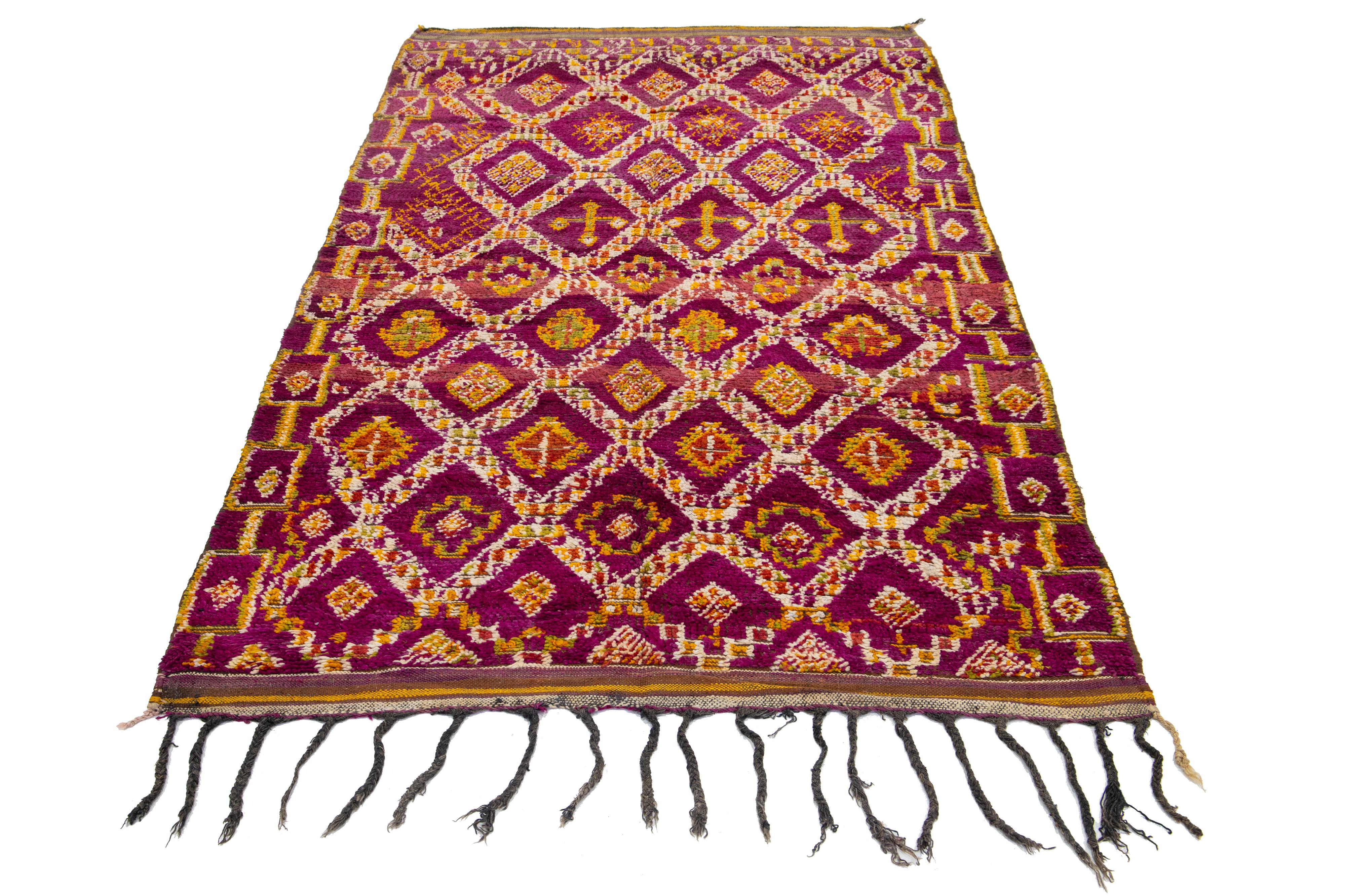 A beautiful, vintage 1960s Moroccan wool rug featuring a purple field adorned with a repeating diamond design. The rug showcases bright yellow, green, orange, and ivory accents throughout its tribal-inspired pattern.

This rug measures 5'2