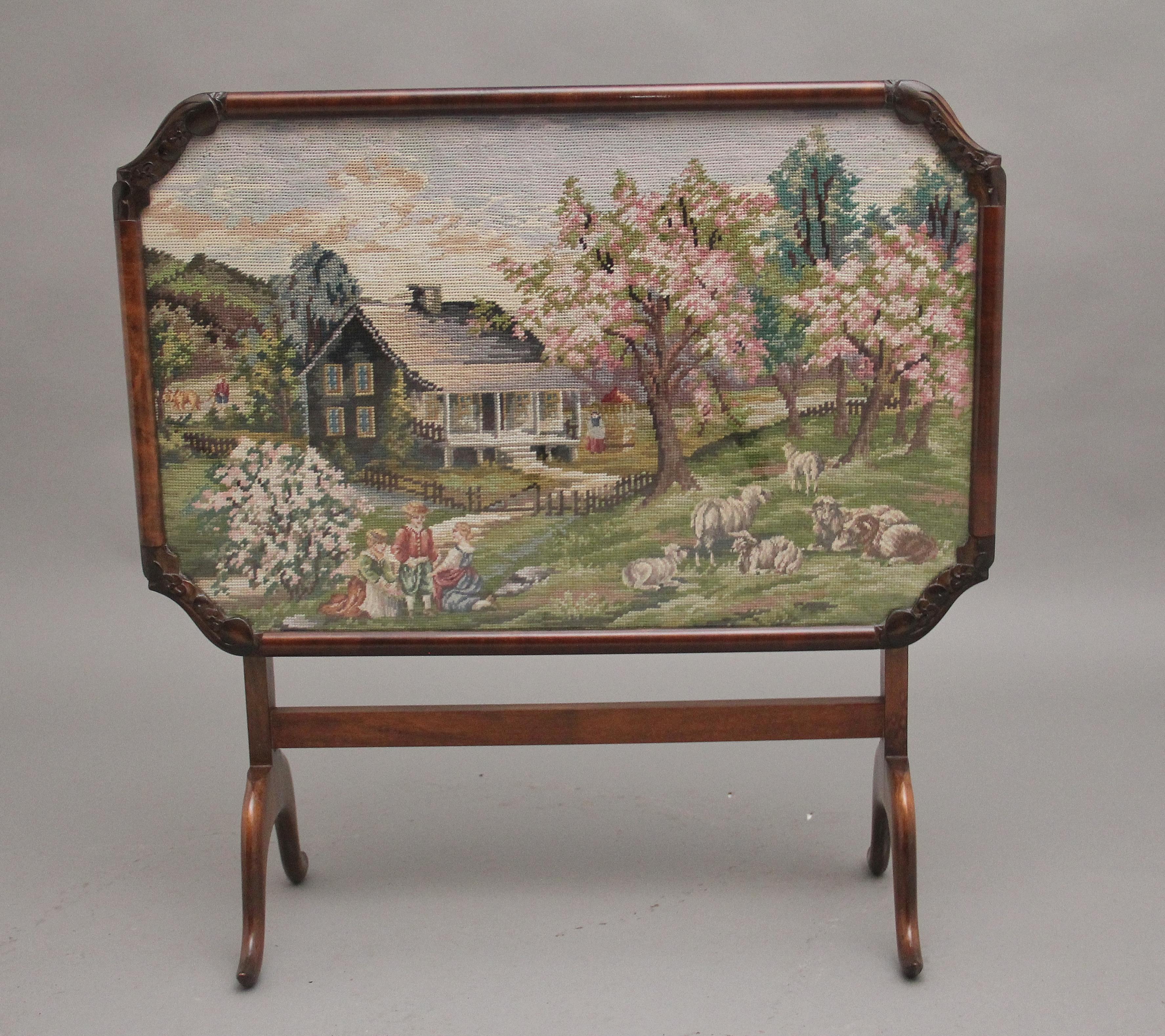 Mid 20th Century walnut fire screen / coffee table, the glazed screen having a needlepoint scene of an idyllic countryside setting, housed within a shaped and carved walnut frame, the screen lifts down so it can be used as a coffee table, supported
