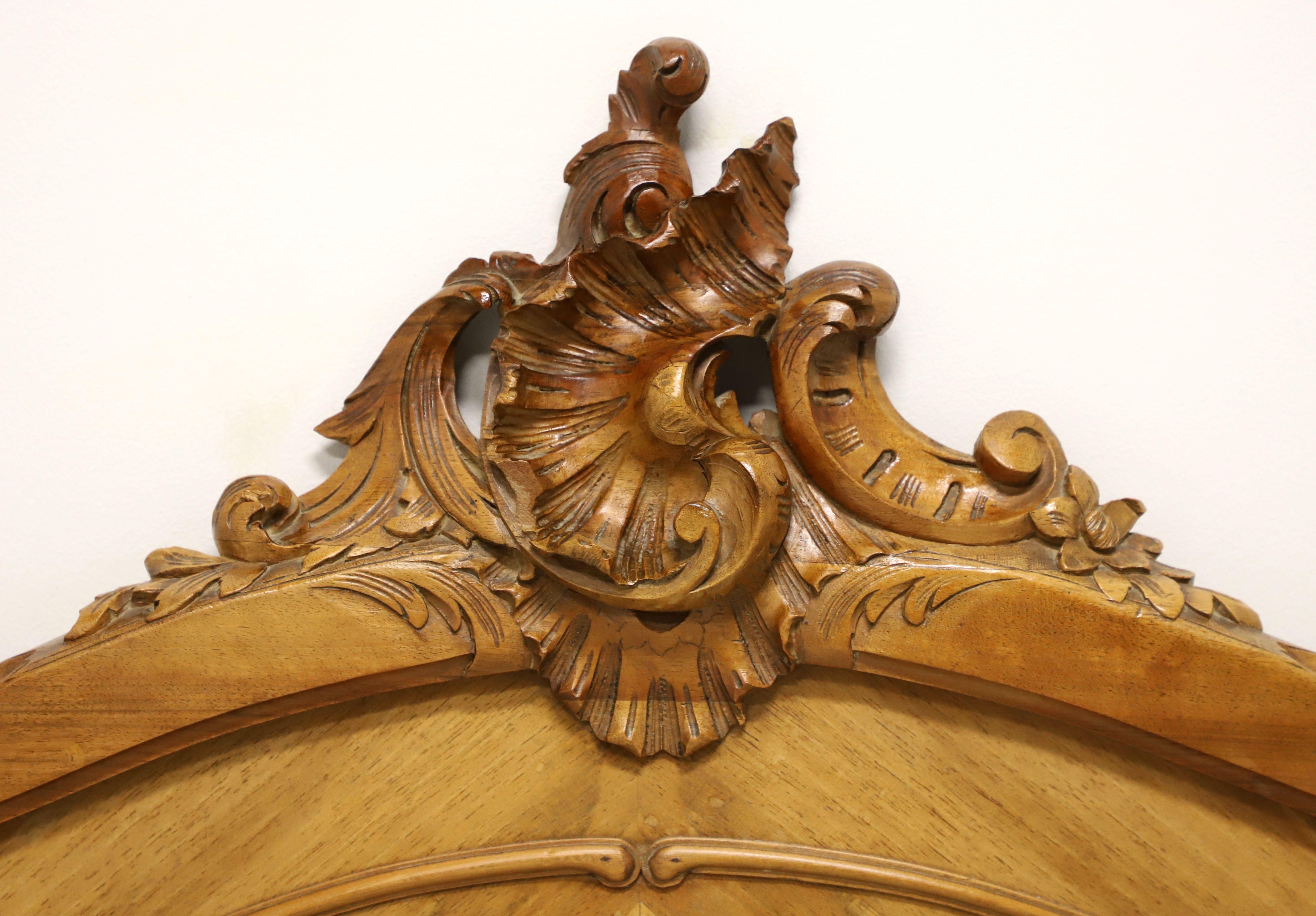 A French Provincial style full size headboard, unbranded. Walnut, or similar nutwood, with a parquetry diamond pattern, arched top with decoratively carved center foliate sheaf, and carved moldings. Made in the USA, in the mid 20th