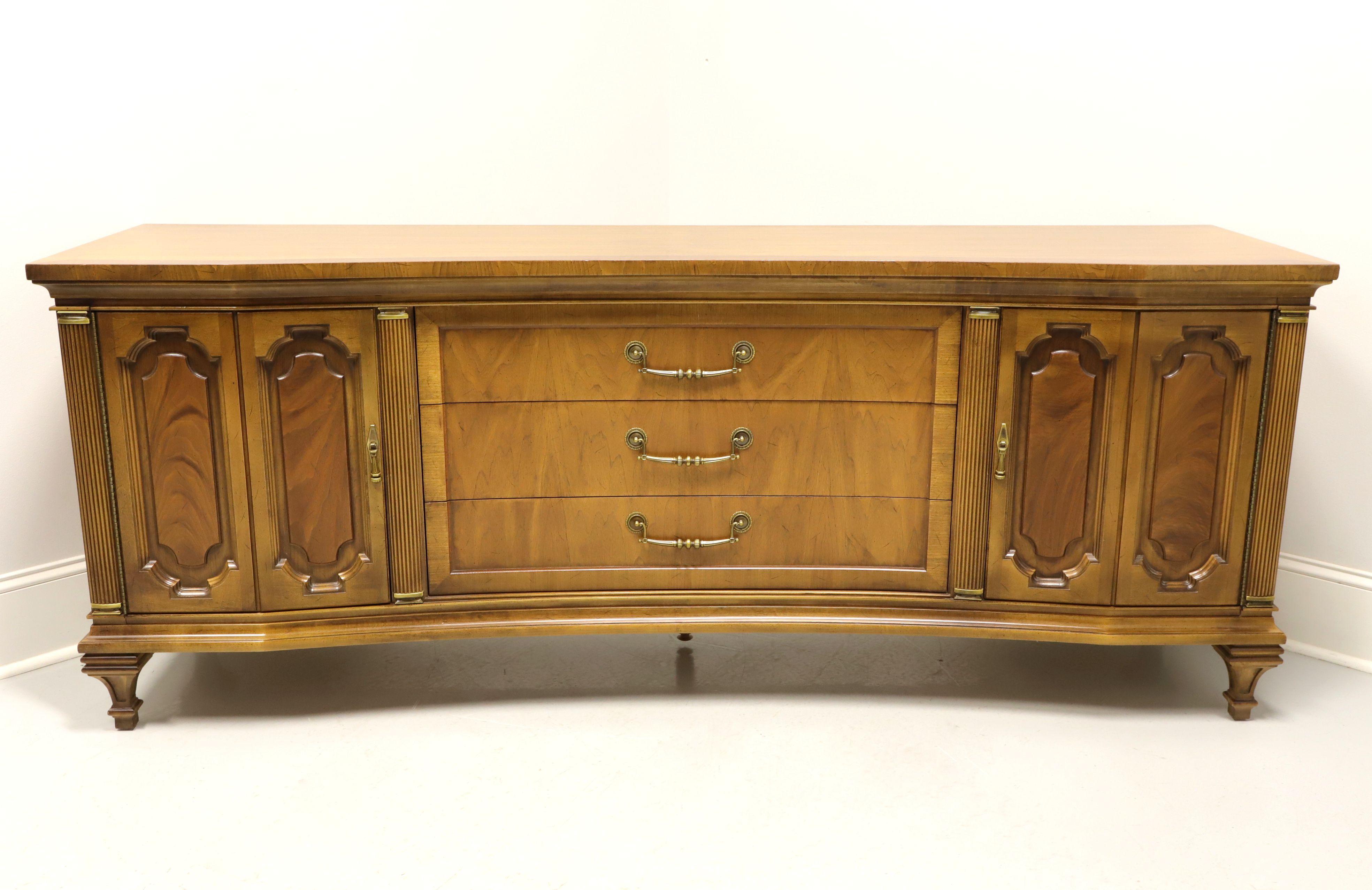 A Hollywood Regency style triple dresser by Unique Furniture, from their Davani Collection. Walnut with banded top, brass hardware, carved door fronts, fluted columns with brass caps flanking the center drawers & at the sides and decoratively carved