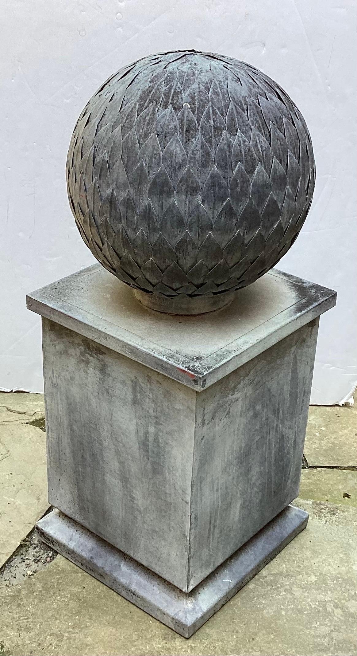 A hand made weather zinc garden sculpture of a sphere on a square plinth base.  The sphere is made of hundreds of leaf shape parts attached to a square base.  40 inches tall, Circa 1970's