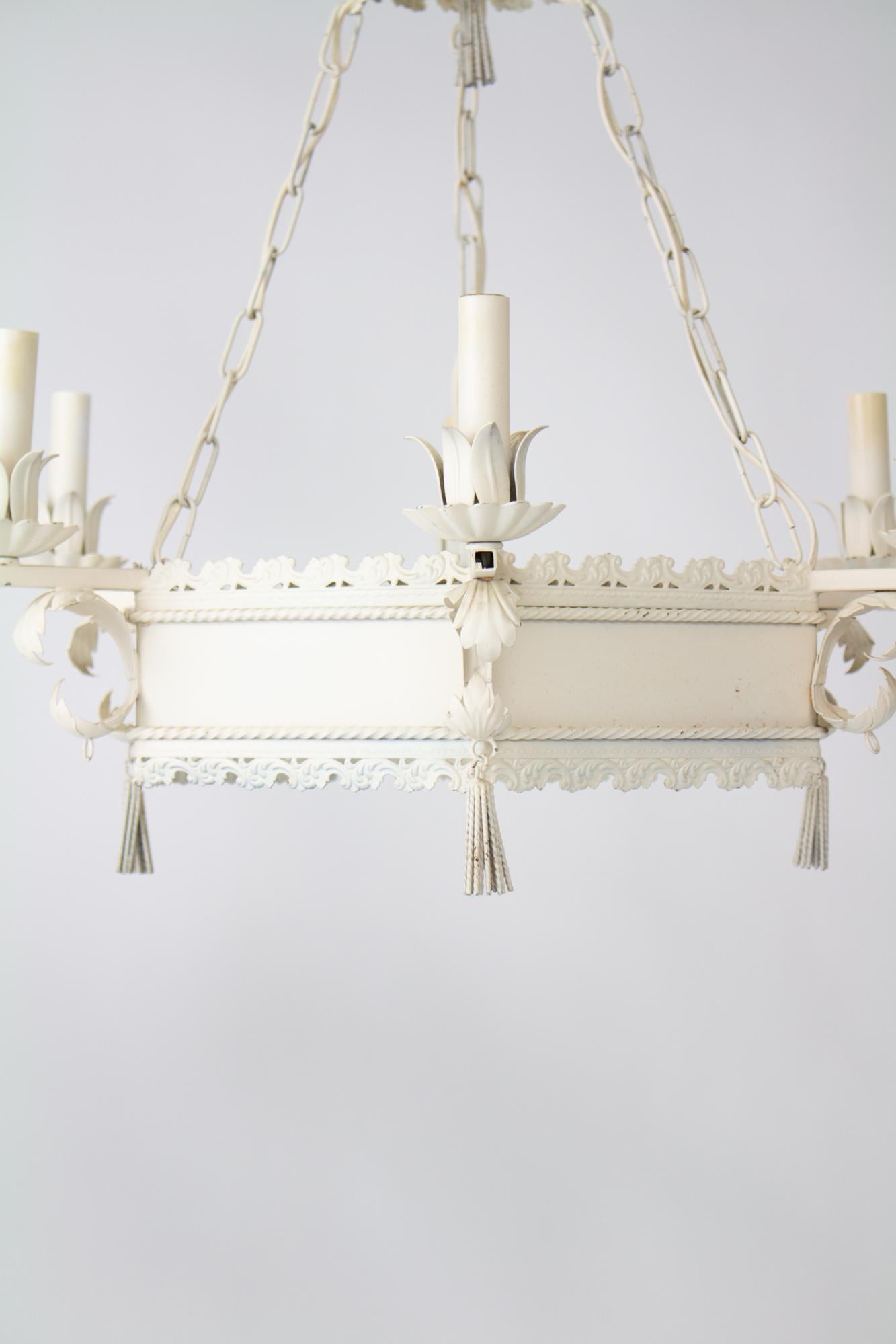 Mid 20th Century white tole chandelier. Hexagonal open body with six lights hangs from a top crown by three chains. Three tassels hang below. White painted finish with some wear and signs of rust. Sold as-is and needs to be rewired. 

Italian, Mid