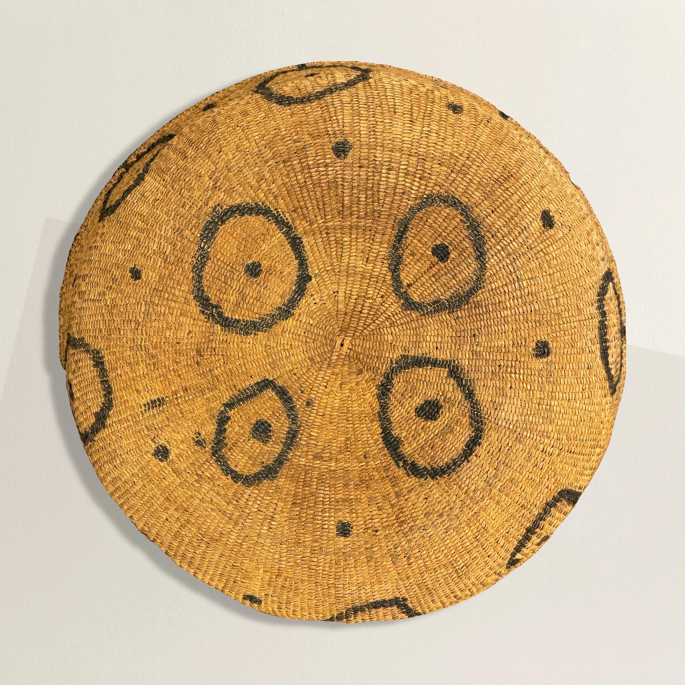 This impressive mid-20th century Yanomami gathering basket is a stunning example of indigenous craftsmanship. It features a large, woven form adorned with distinctive circles, each with a central dot, meticulously drawn with black ash. The design is