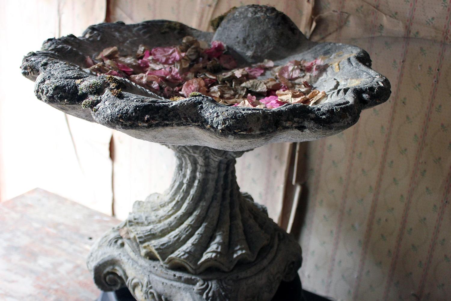 The well modelled cast stone bird bath, modelled as an open scallop shell on a spiral turned socle column and plinth base; with an added associated ebonized plinth base, the whole surviving from the mid-20th century.
 
The bird bath is in three