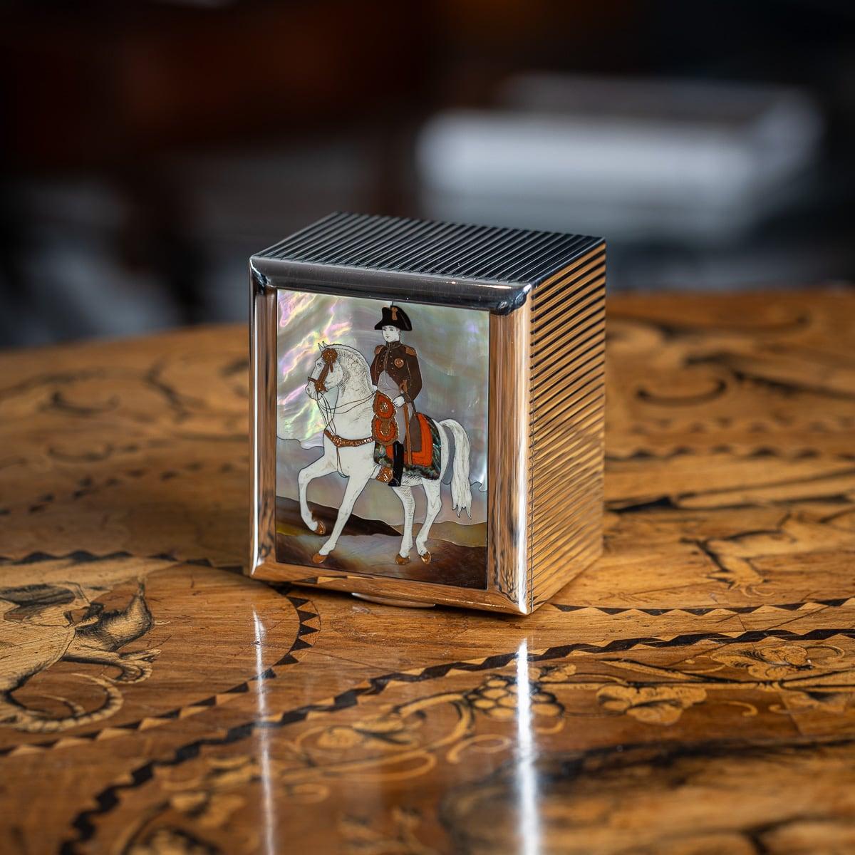 Caja francesa de mediados del siglo XX de plata maciza, oro de 18 quilates y nácar, fabricada en París y vendida por Dunhill. De forma rectangular, la tapa presenta un intrincado panel con incrustaciones que representa a Napoleón I a lomos de su