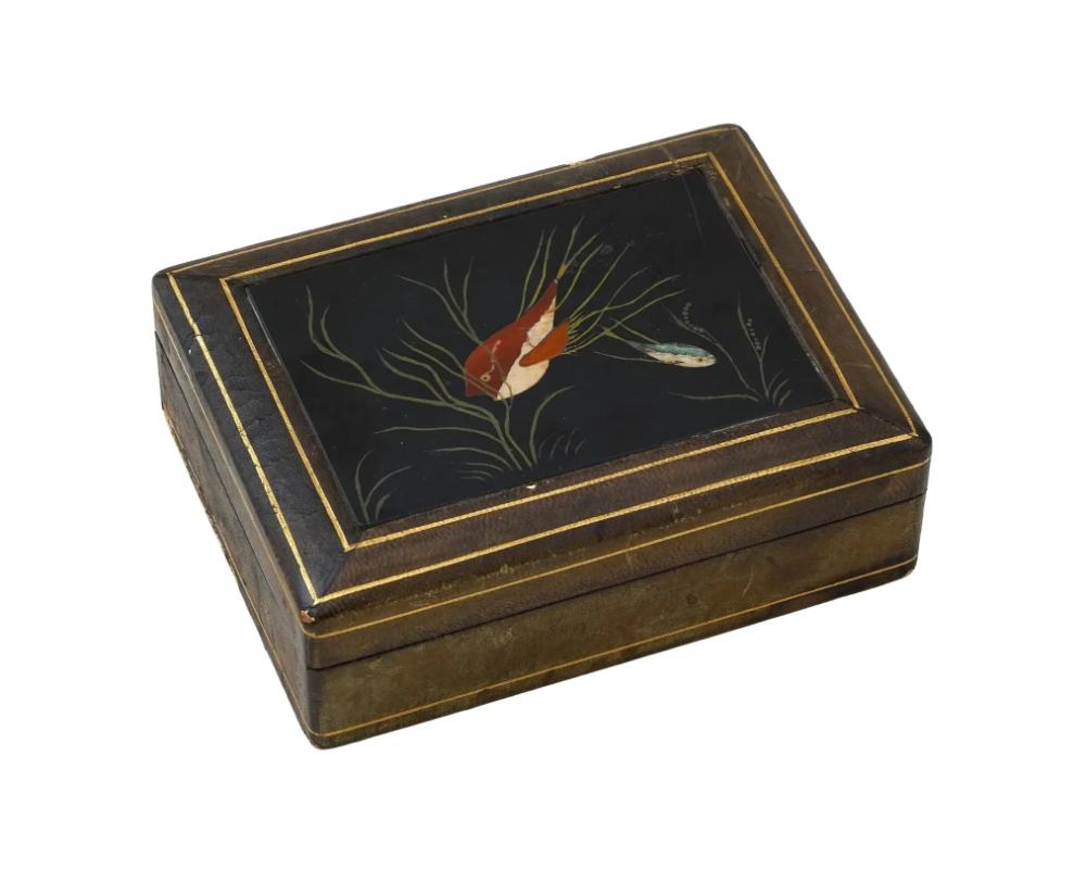 Una caja de madera tapizada en piel italiana Firenze de mediados del siglo XX. La tapa de la caja está realizada en técnica de pietra dura, una incrustación de piedras de colores cortadas y encajadas, muy pulidas. La obra representa un pez en un