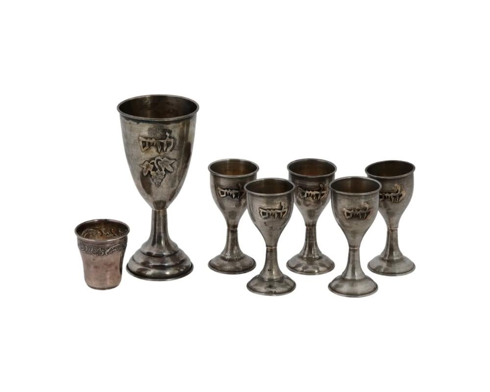 A lot of mid-20th century sterling silver kiddush cups. Presumably of German or Austrian origin. A set of five items and a single larger cup. The footed cups are decorated with embossed winegrape decor and inscriptions Cheers in Hebrew. Marked 935