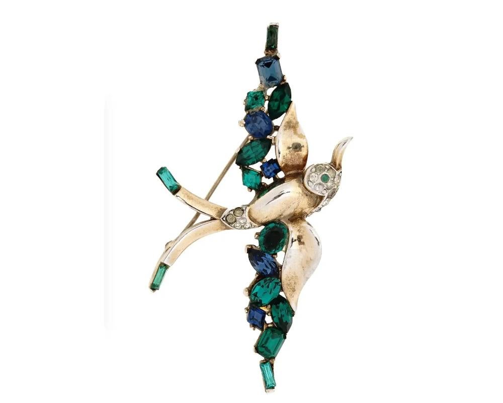 A mid-20th century golden bird brooch garnished with rhinestones and blue and green faceted stones. Hallmark Trifari is on the backside. Collectible Jewelry And Fashion Accessories For Women.

Dimensions: Size: 2 7/8 x 2 in. All measurements are