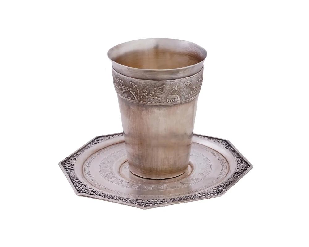 A set of mid-20th century Vietnamese silver tableware, a cup and a saucer. Tall cup with an embossed band on top depicting a frieze composition, village view with a peasant. Octagonal saucer with pierced rim decor, etched ornaments and central