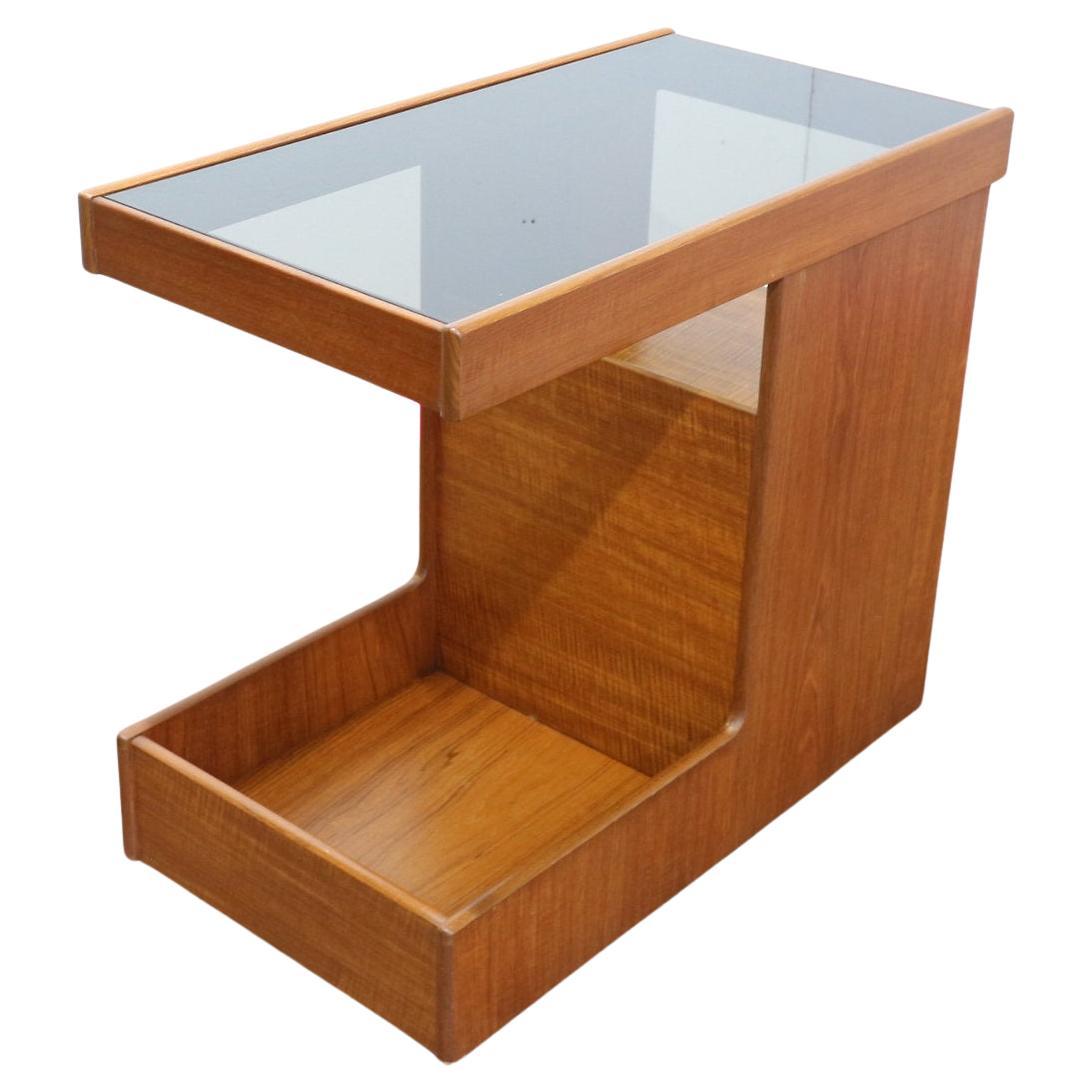 Eleva la tua esperienza di intrattenimento con questo carrello da bar in teak del Mid Century Modern. Questo sofisticato carrello bar è dotato di un elegante piano in vetro e di un apposito vano portabottiglie, che unisce forma e funzionalità senza