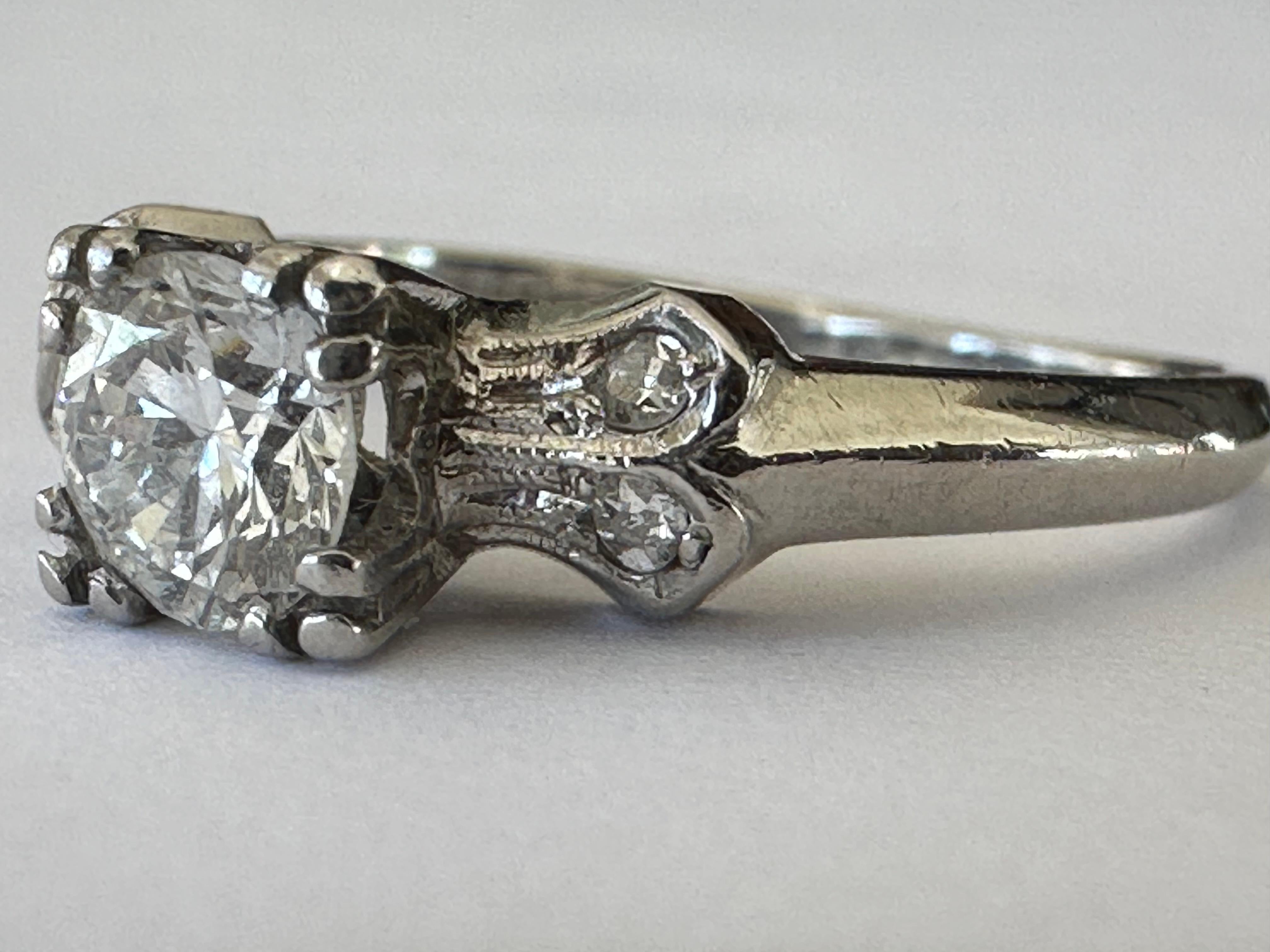 An Old European-cut diamond center stone measuring approximately 0.50 carat, G color VS clarity, is set between hand engraved shoulders studded with four single cut diamonds. Set in platinum. Circa 1950s. 