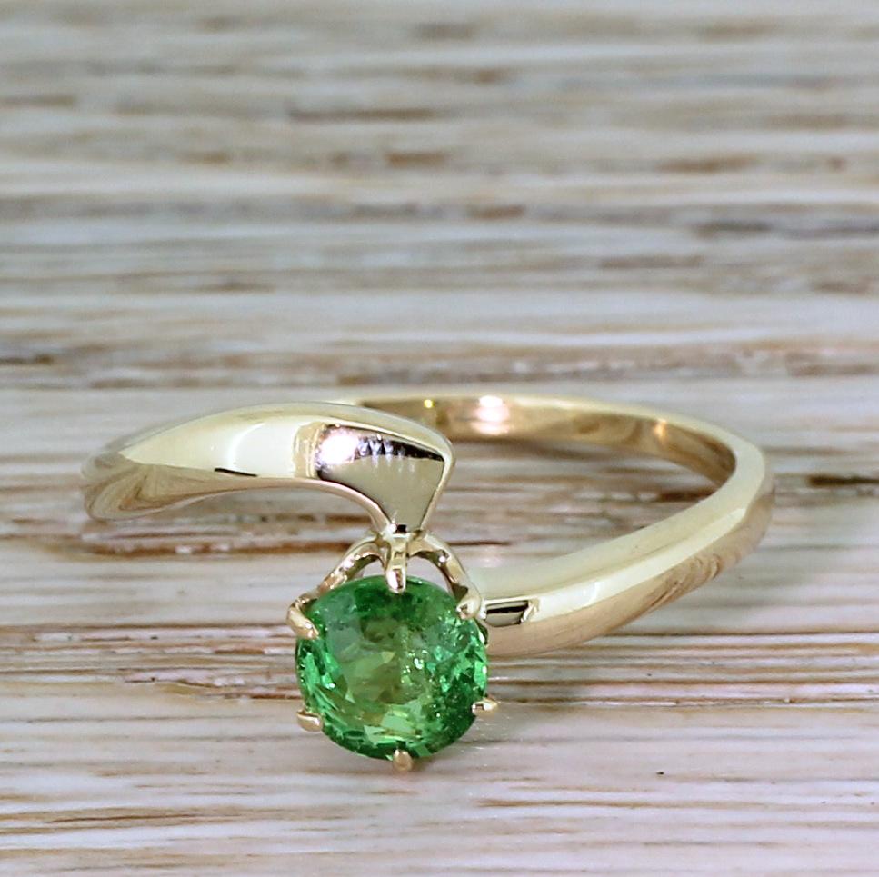 A fabulous and unique demantoid garnet ring. The garnet displays an intense, electric yellowish green that is so bright it seems almost other-worldly. The stone is secured in a six claw coronet collet that sits within a stylishly asymmetrical