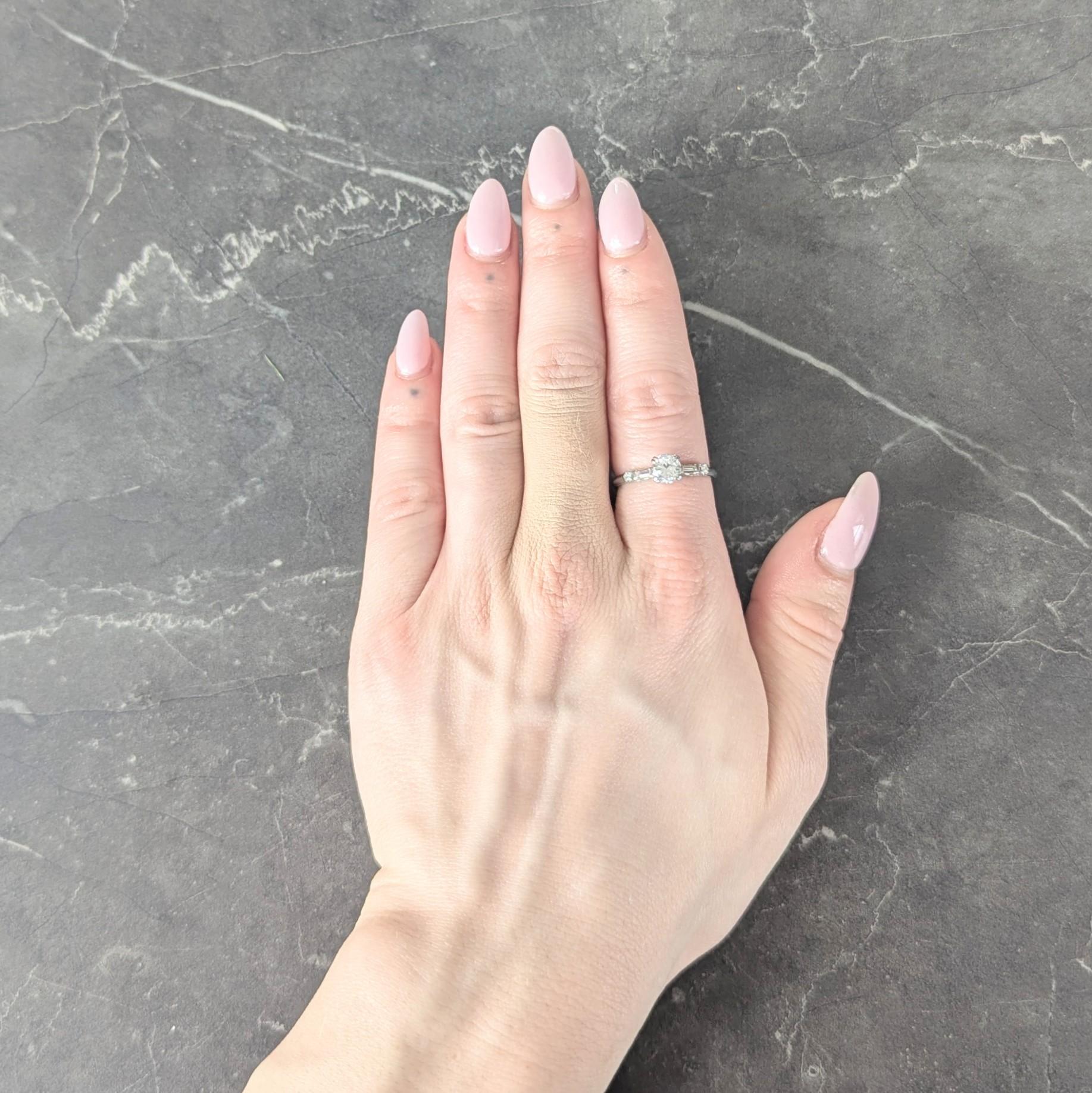 Centering an transitional cut diamond weighing 0.71 carats total - H color with VS2 clarity
Set with tri-split prongs in a square form basket with pierced fishtail motif profile
Flanked by cathedral shoulders set with baguette and single cut