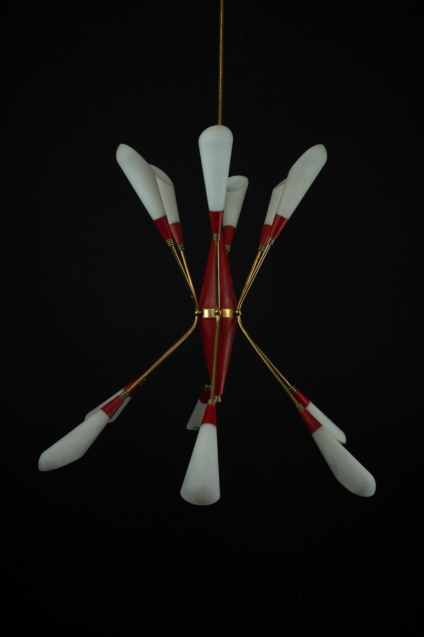 Lustre à 12 lumières du milieu du siècle à la manière de Stilnovo, Italie, années 1950. Structure en laiton avec des éléments en métal laqué rouge et des abat-jours en verre opalin allongé, disposés dans une composition radiale dynamique. Un exemple