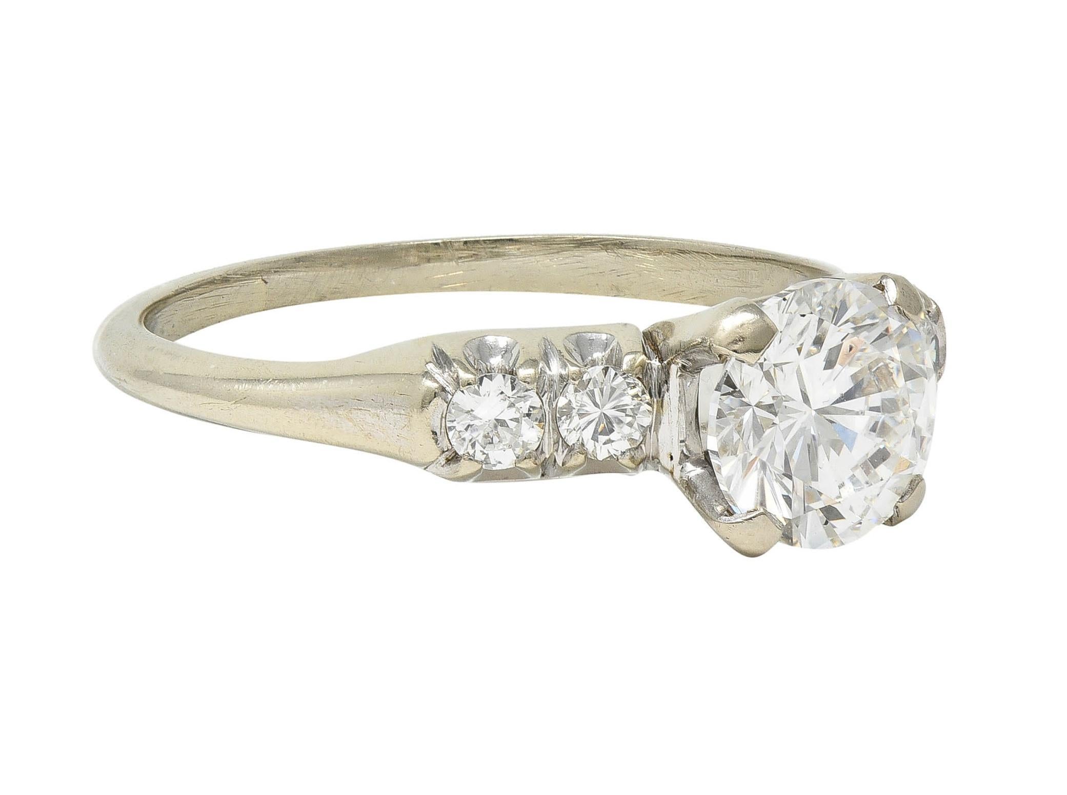 Centering a 1.00 carat round brilliant cut diamond - E in color with SI1 clarity
Prong set in a basket and flanked by prong set round brilliant cut diamonds
Weighing approximately 0.20 carat total - well matched to center
Completed by fishtail motif