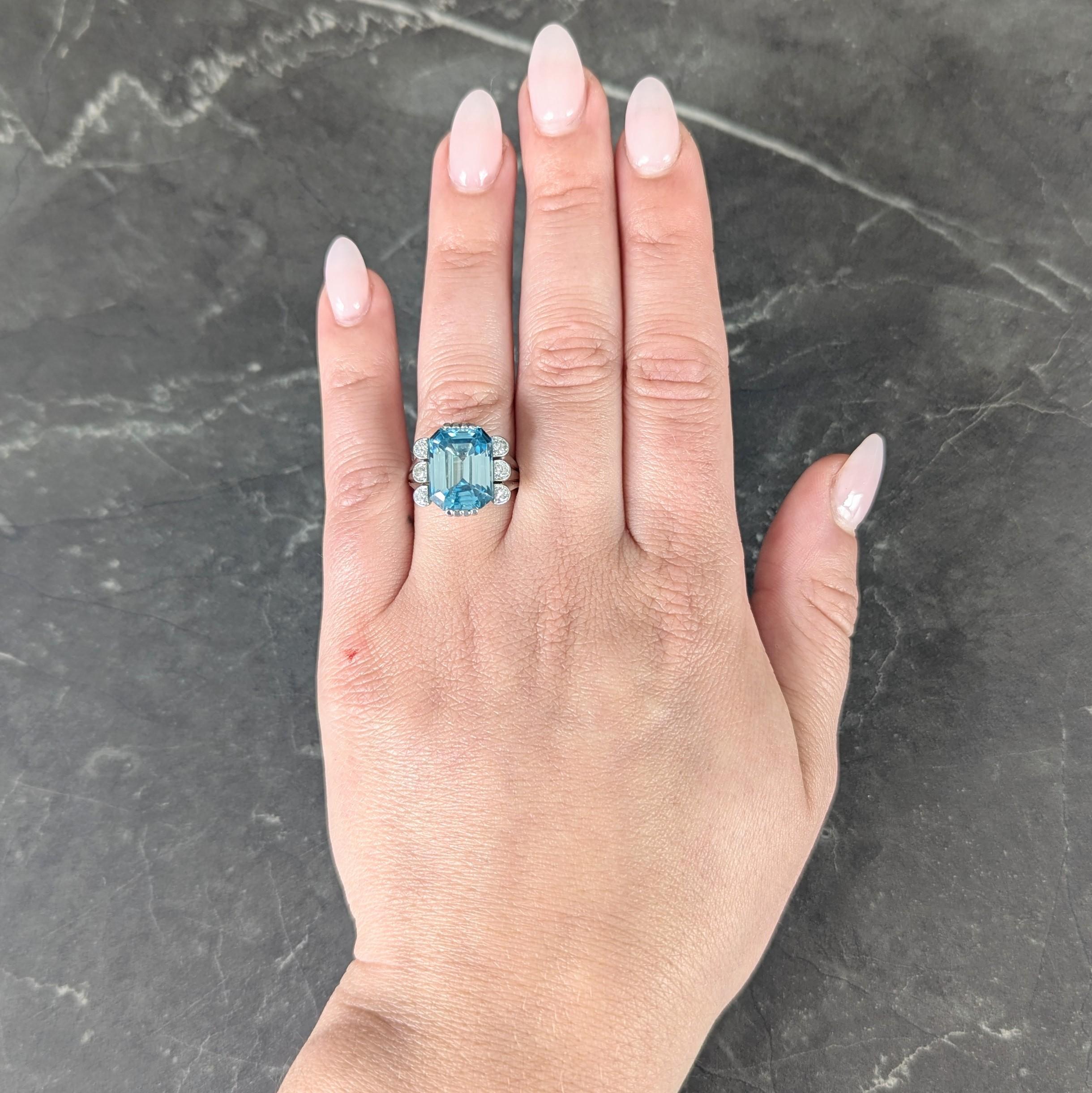 Centering an emerald cut zircon weighing approximately 11.54 carats - transparent medium greenish blue
Set with grooved wide prongs and flanked by tri-split scalloped shoulders
Bead set north to south with rows of transitional cut diamonds
Weighing