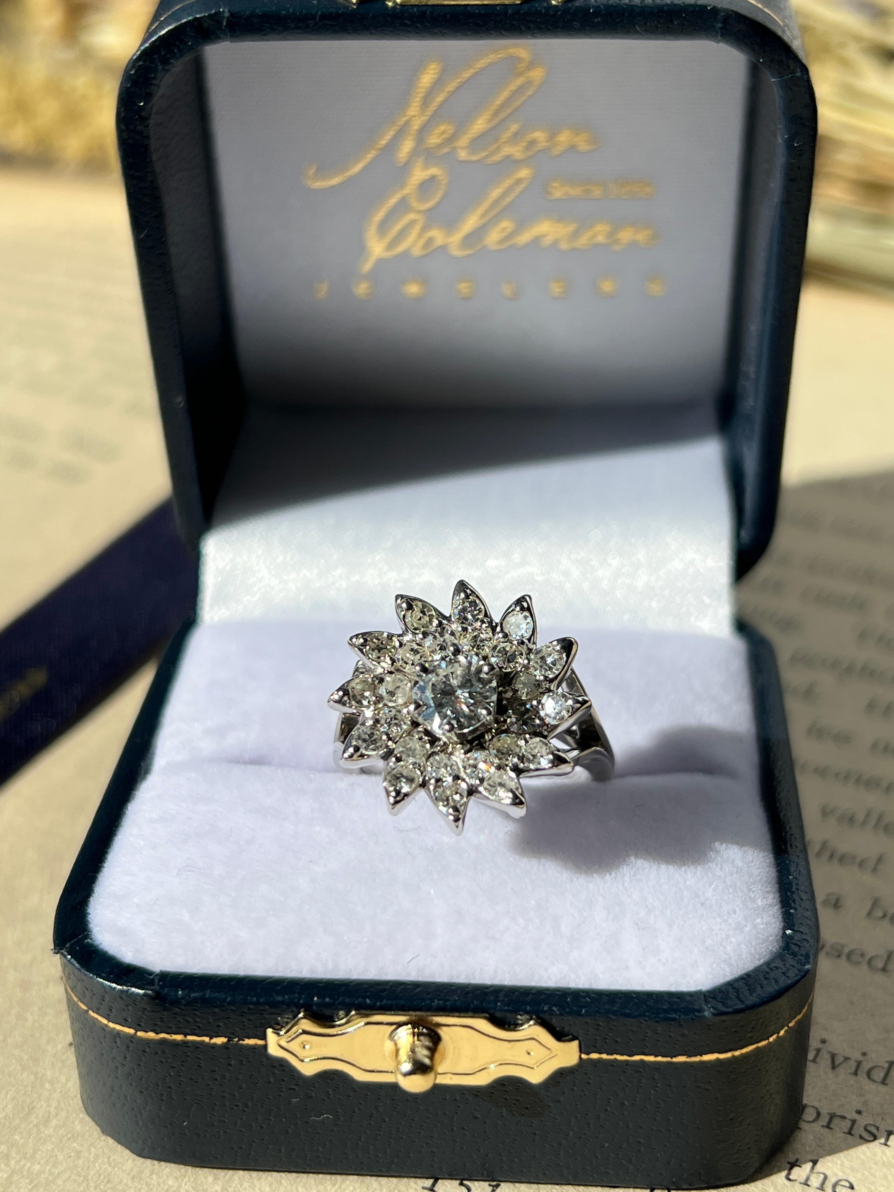 Questo anello in oro bianco 14 carati del 1950 cattura il fascino romantico del design di metà secolo. Un diamante rotondo brillante da 0,57 carati, di colore H e purezza VS2, si trova al centro di un delicato motivo floreale che evoca il glamour