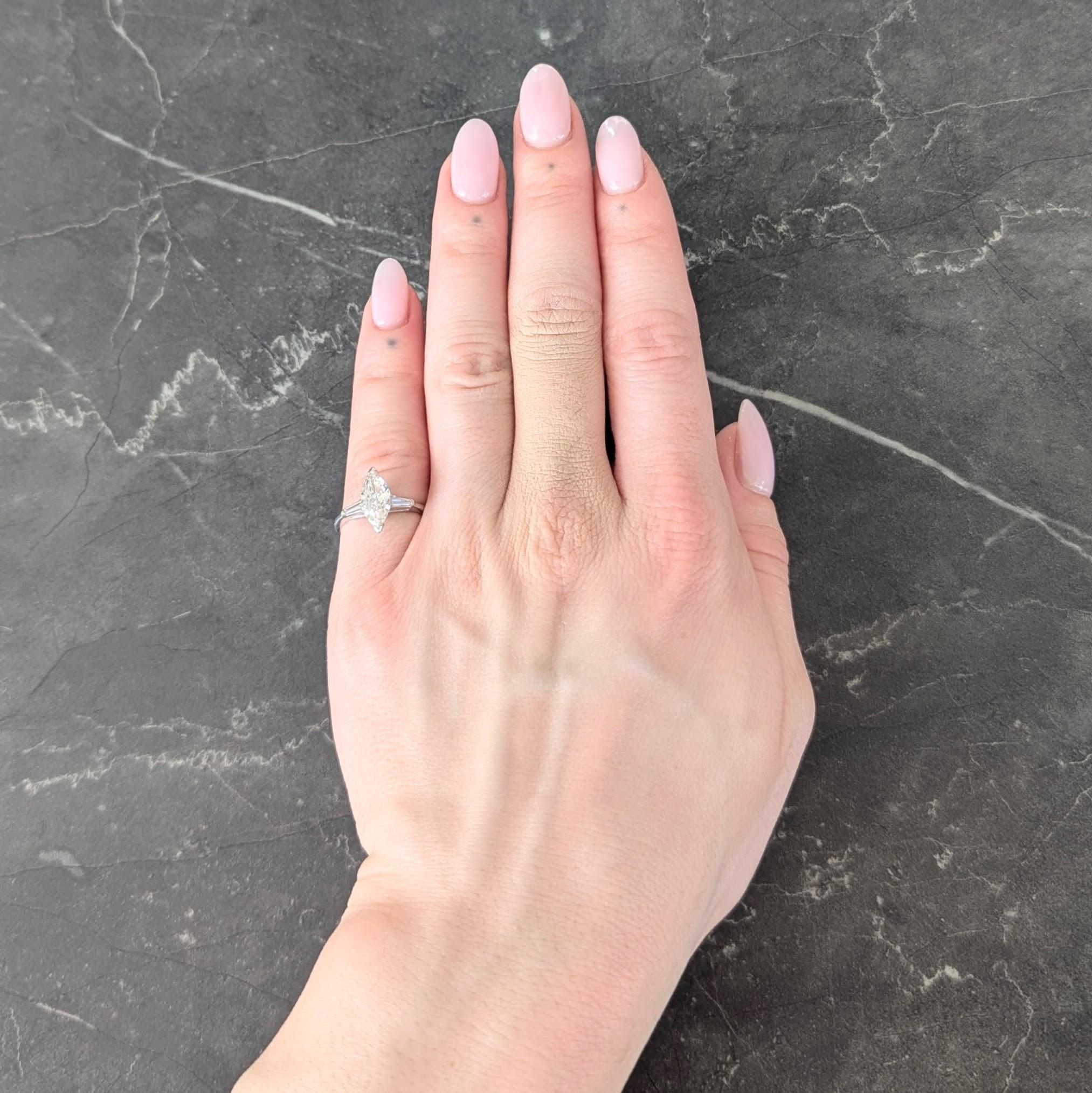 Centering a marquise cut diamond weighing approximately 1.19 carats - H color with VS2 clarity
Prong set north to south in basket and flanked by cathedral shoulders
Bar set with tapered baguette cut diamonds - well matched to center
Weighing