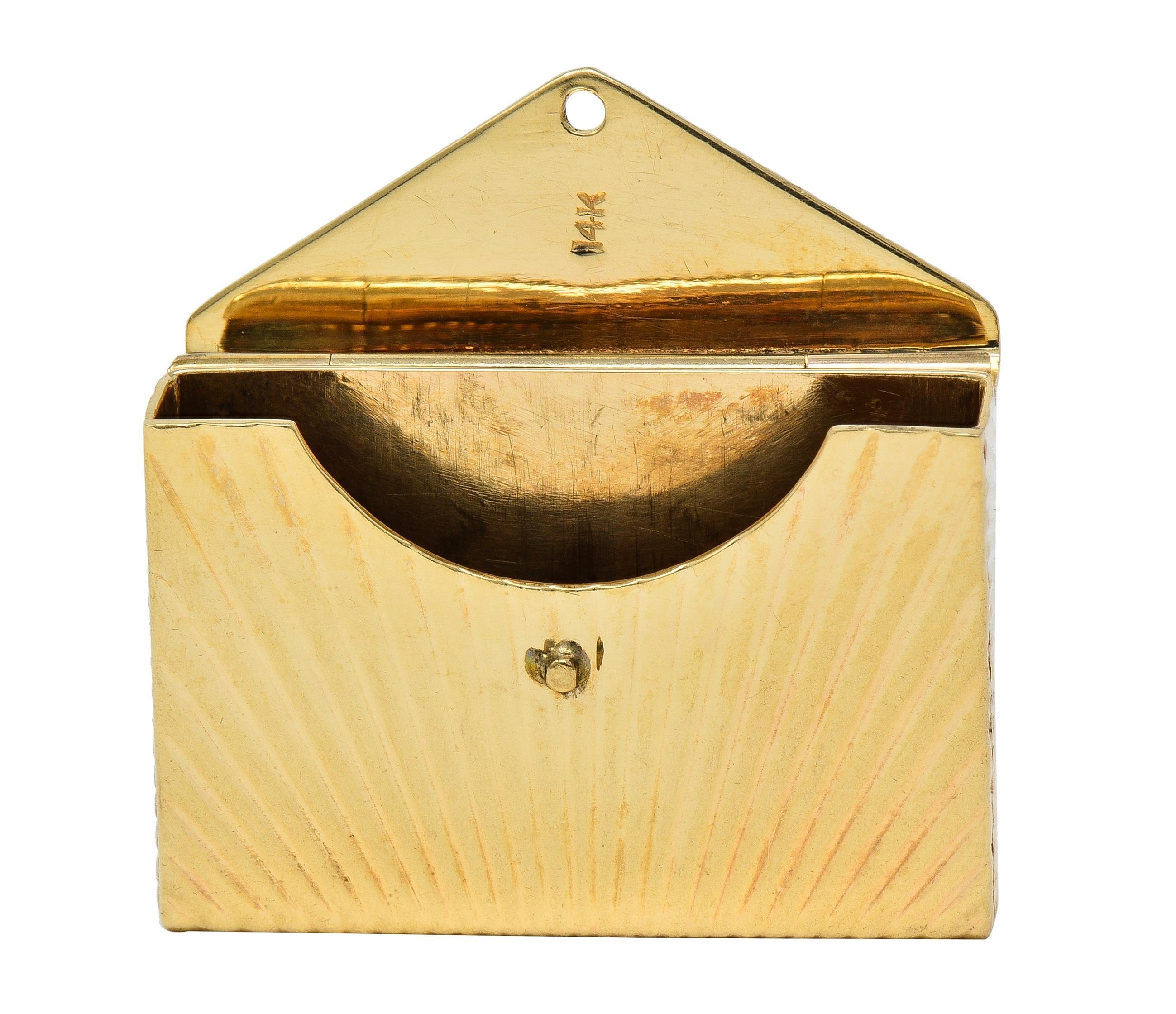 Conçu comme une enveloppe stylisée cannelée avec un motif radial éclaté
L'une des faces comporte un timbre vierge et l'autre un rabat à charnière.
S'ouvre pour révéler un compartiment
Complété par une balle d'anneaux de saut
Estampillé pour l'or 14