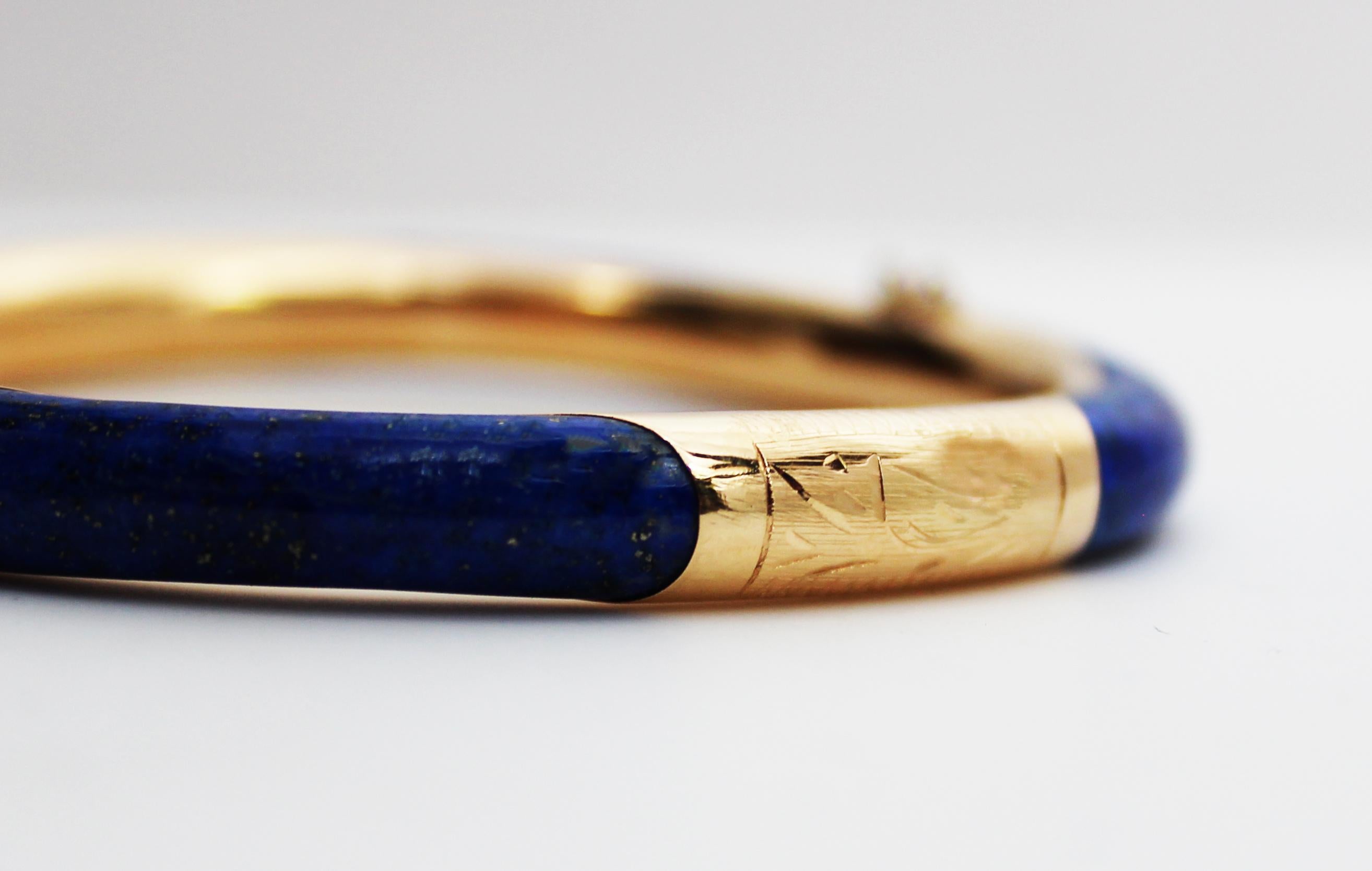 This is an elegant mid-century 14k yellow gold hinged bangle featuring gorgeous inlays of blue lapis! The bangle has a sleek rounded look and a dramatic gold and royal blue color scheme that is impossible to miss. The bangle is hinged in such a way