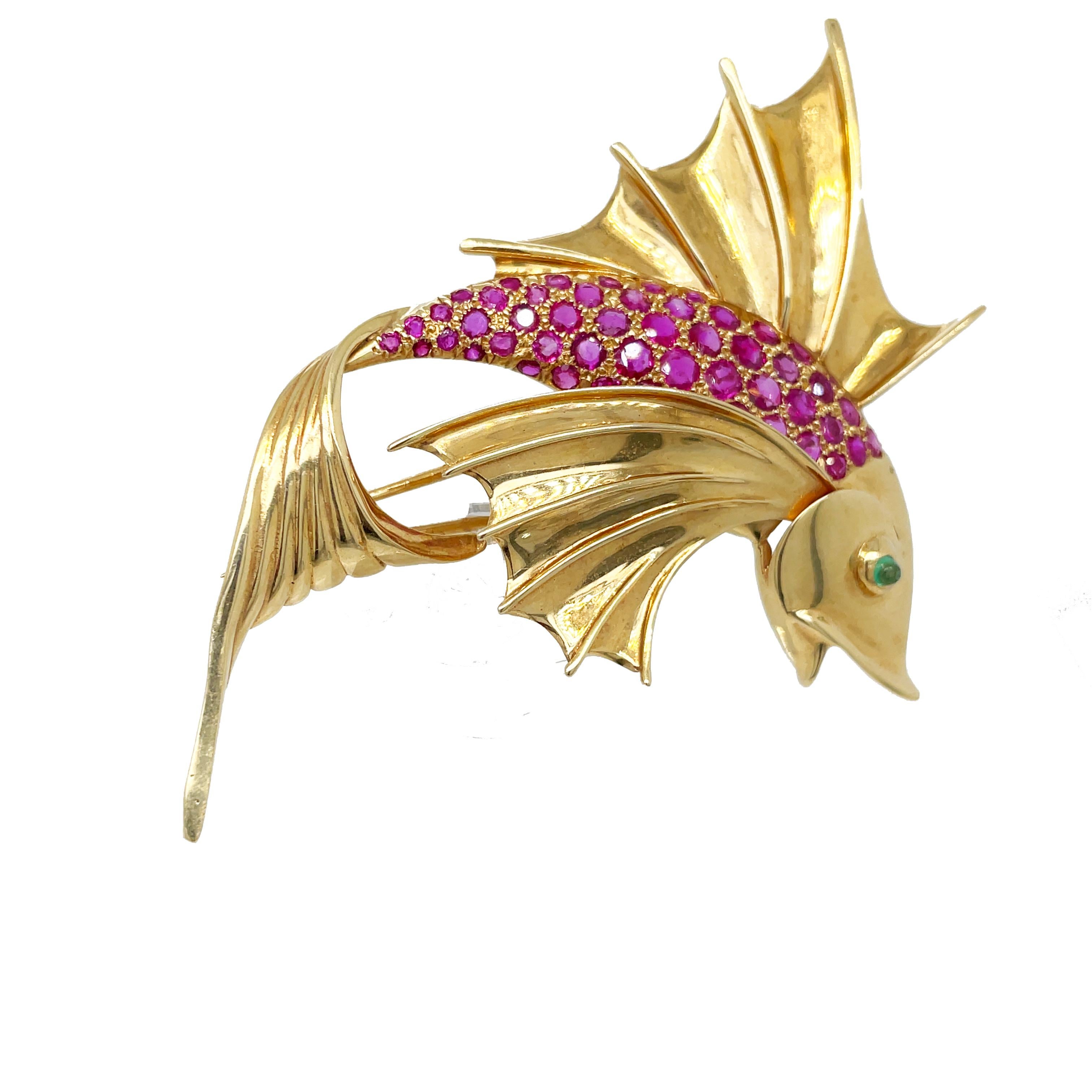 This is an absolutely show-stopping 1960s fish pin set in 14K yellow gold that features gorgeous dazzling rubies across the body and an emerald eye. The intricate detail and craftmanship of this pin are truly extraordinary. With an approximate total