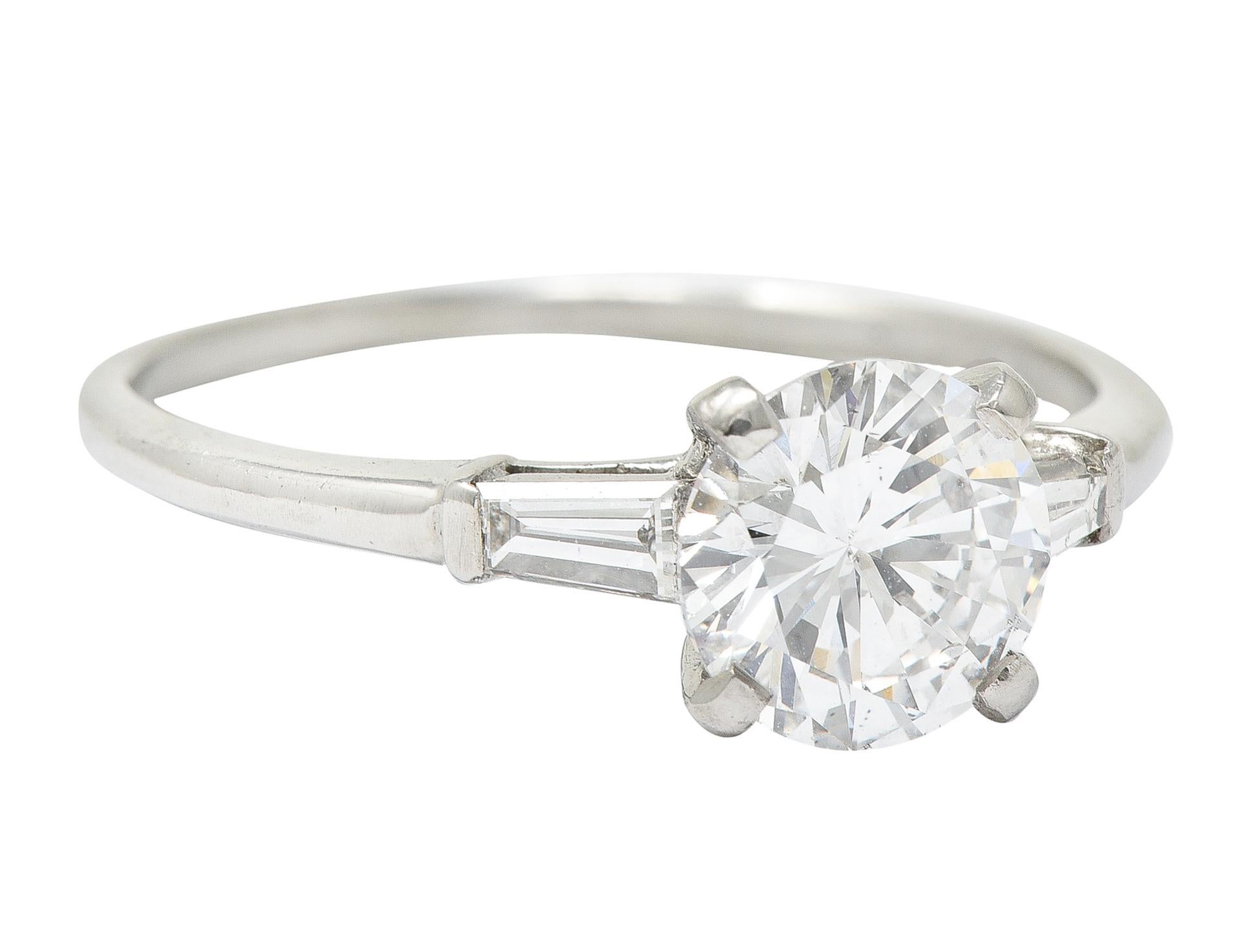 Engagement ring centers a round brilliant cut diamond weighing 1.33 carats total - D color with SI2 clarity. Prong set in basket and flanked by tapered baguette cut diamonds bar set in cathedral shoulders. Weighing approximately 0.24 carat total -