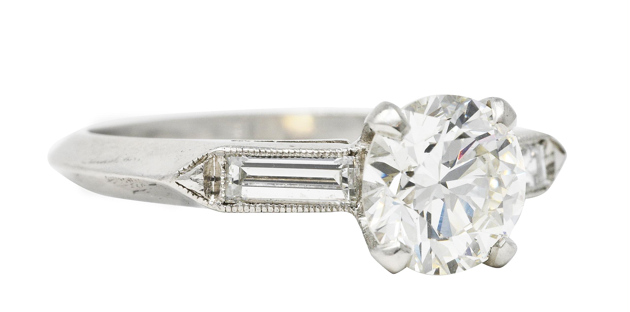 Ring centers a round brilliant cut diamond weighing 1.36 carats total - J in color with VVS1 clarity. Prong set in a basket and flanked by cathedral shoulders channel set with baguette cut diamonds. Weighing approximately 0.22 carat total - well