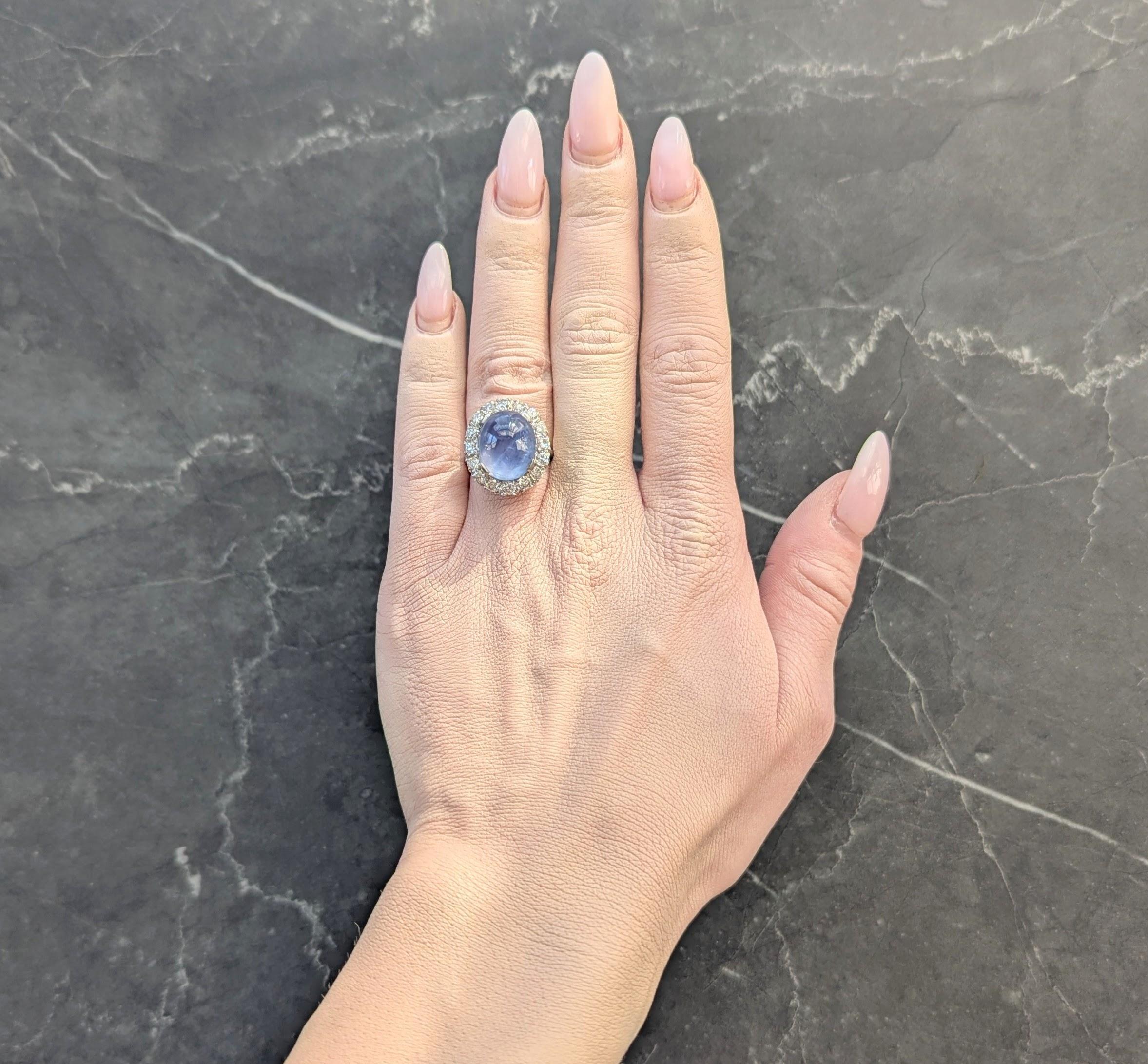 Centering an oval shaped sapphire cabochon weighing approximately 15.15 carats
Transparent light blue in color and displaying a moderate six point asterism
Set by wide tab prongs with a transitional cut diamond halo surround
Weighing approximately