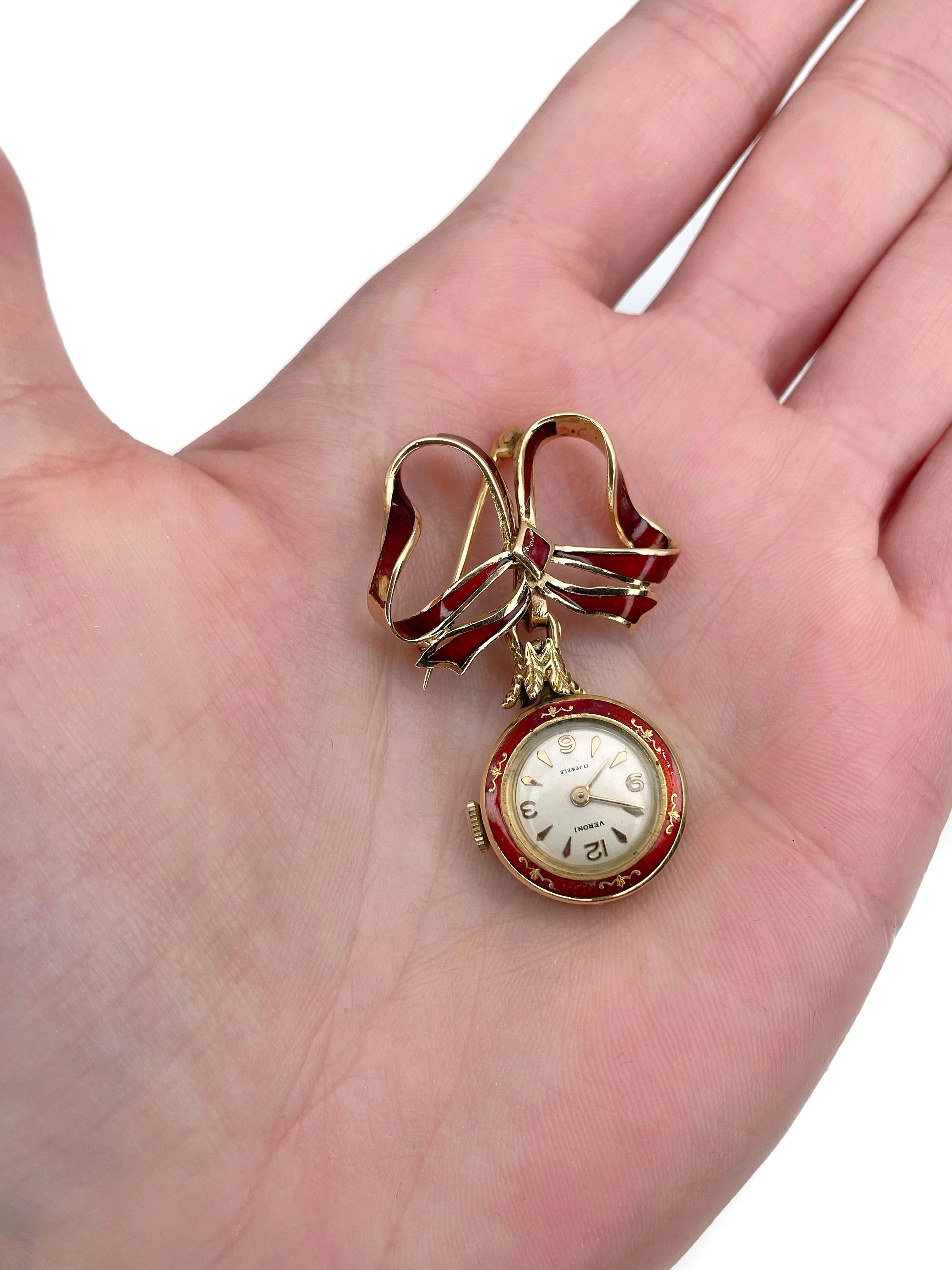 This is an elegant bow brooch with a watch. It is crafted in 18K yellow gold. Circa 1960. 

The piece is adorned with red enamel.
The watch is working. Signed “Veroni. 17 Jewels”

Has a safe closure. 

Weight: 11.68g
Size: 4.5x3cm
Watch diameter:
