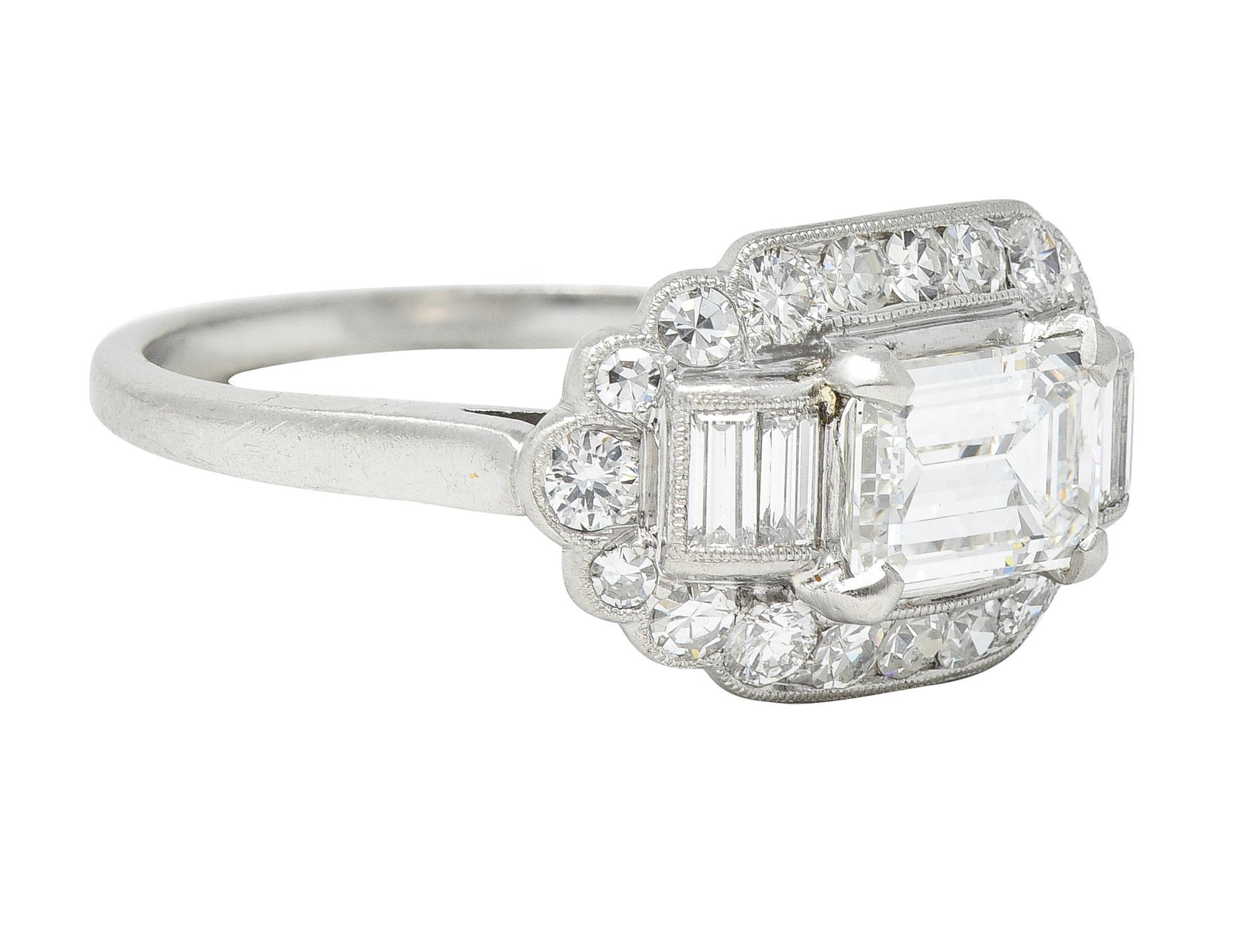 Centering an emerald cut diamond weighing 1.03 carats - G color with VS1 clarity
Prong set east to west and flanked by baguette cut diamonds 
Weighing approximately 0.24 carat total G color with VS1 clarity
Bar set with a recessed oval shaped halo