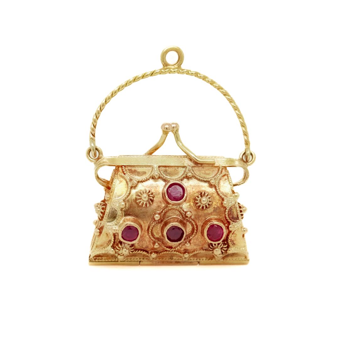 A fine vintage figural purse charm or pendant.

In 18k gold.

Bezel-set with 8 round cut rubies. 

In the form of a purse or lady's handbag that opens with a hinge to the base, a snap closure that closes tightly, and applied rope and granulation