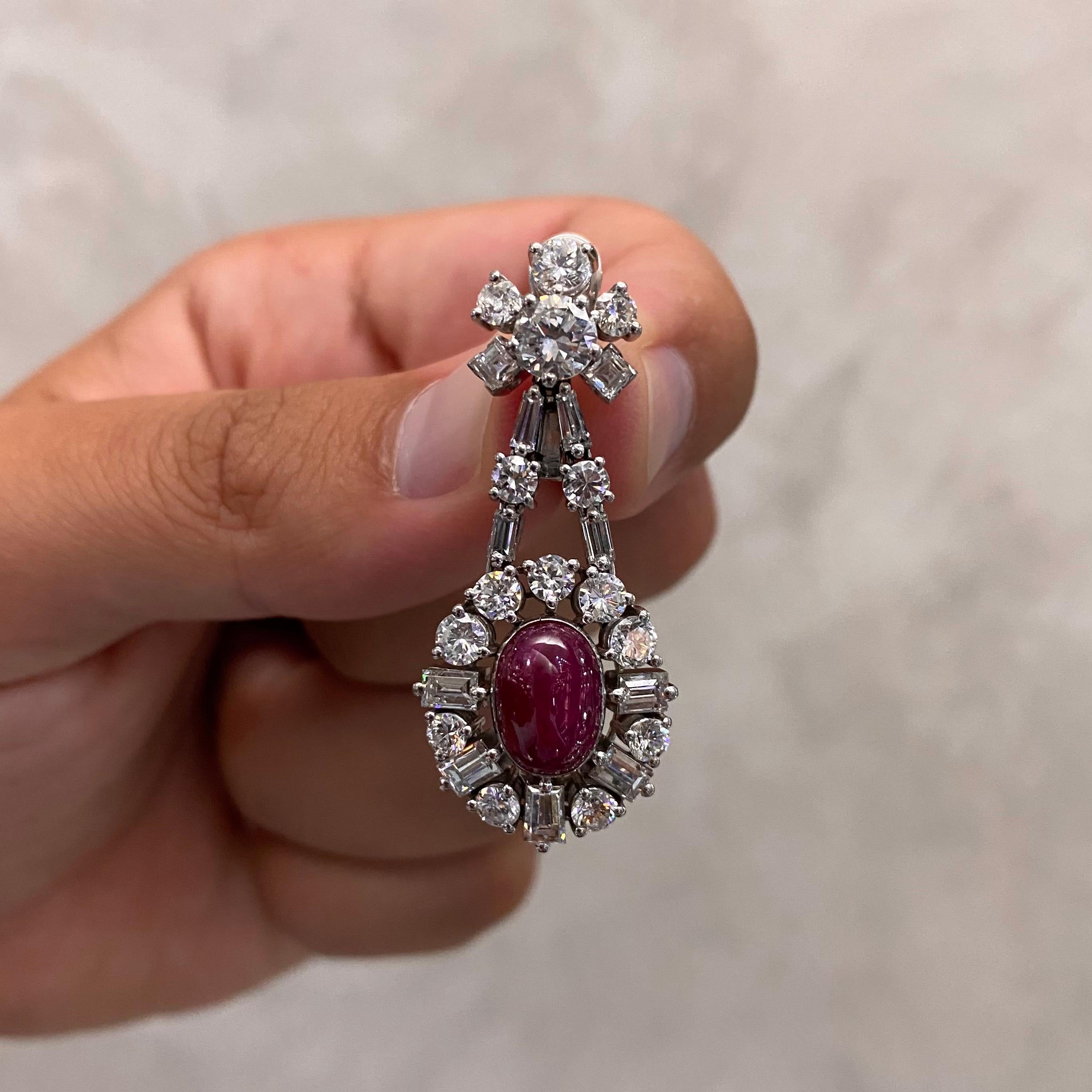 A pair of Mid-Century ruby and diamond earrings in platinum, Portuguese, 1960s. Each earring is composed of a diamond floral cluster surmount suspending an oval cabochon Burmese ruby and diamond cluster drop. The diamond surmount is designed with a
