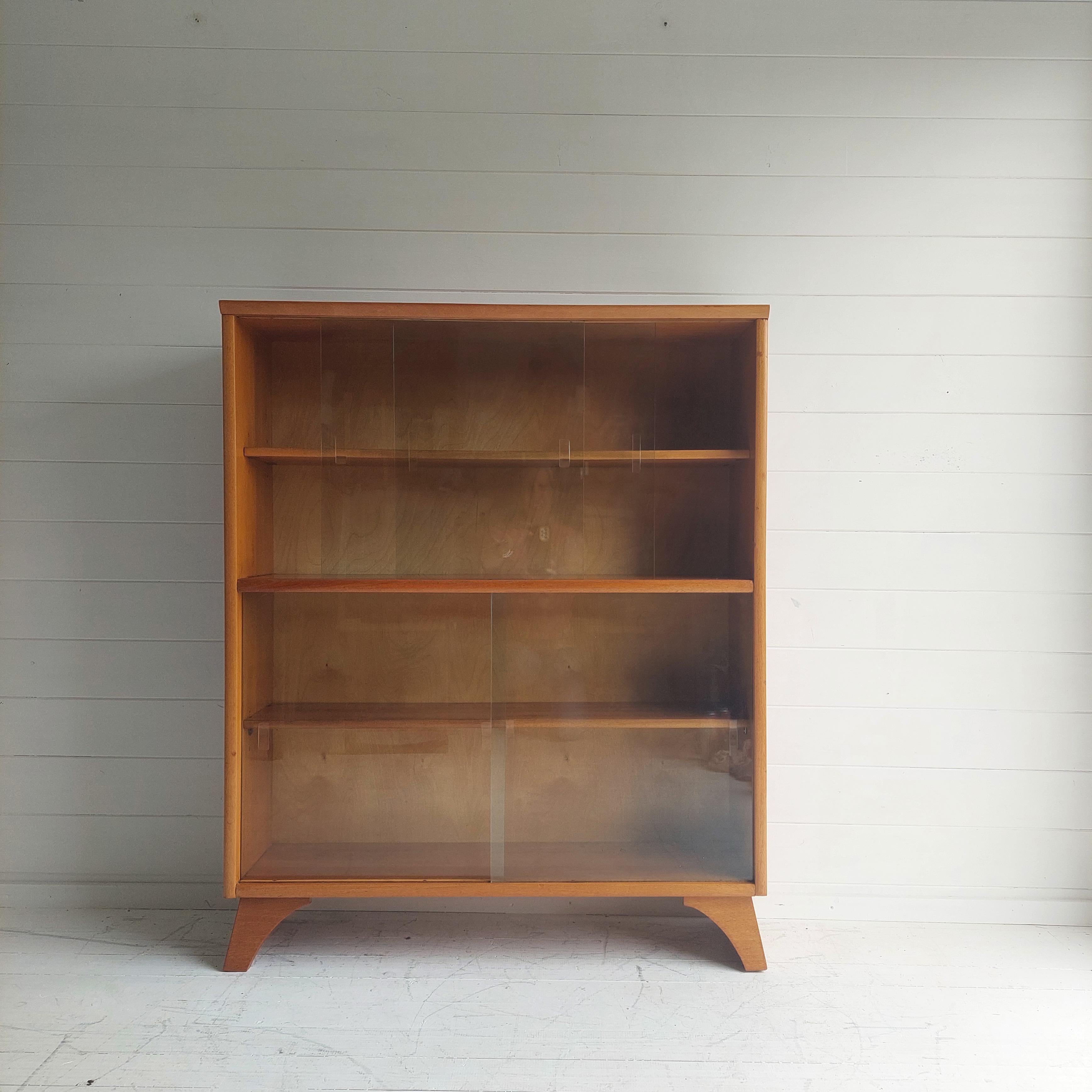 An excellent example of an original mid century double height glazed bookcase/ unit produced by Herbert E Gibbs.
Produced in the 1960’s this is solid teak, completely original and in excellent condition.

It has both of its original sliding glass