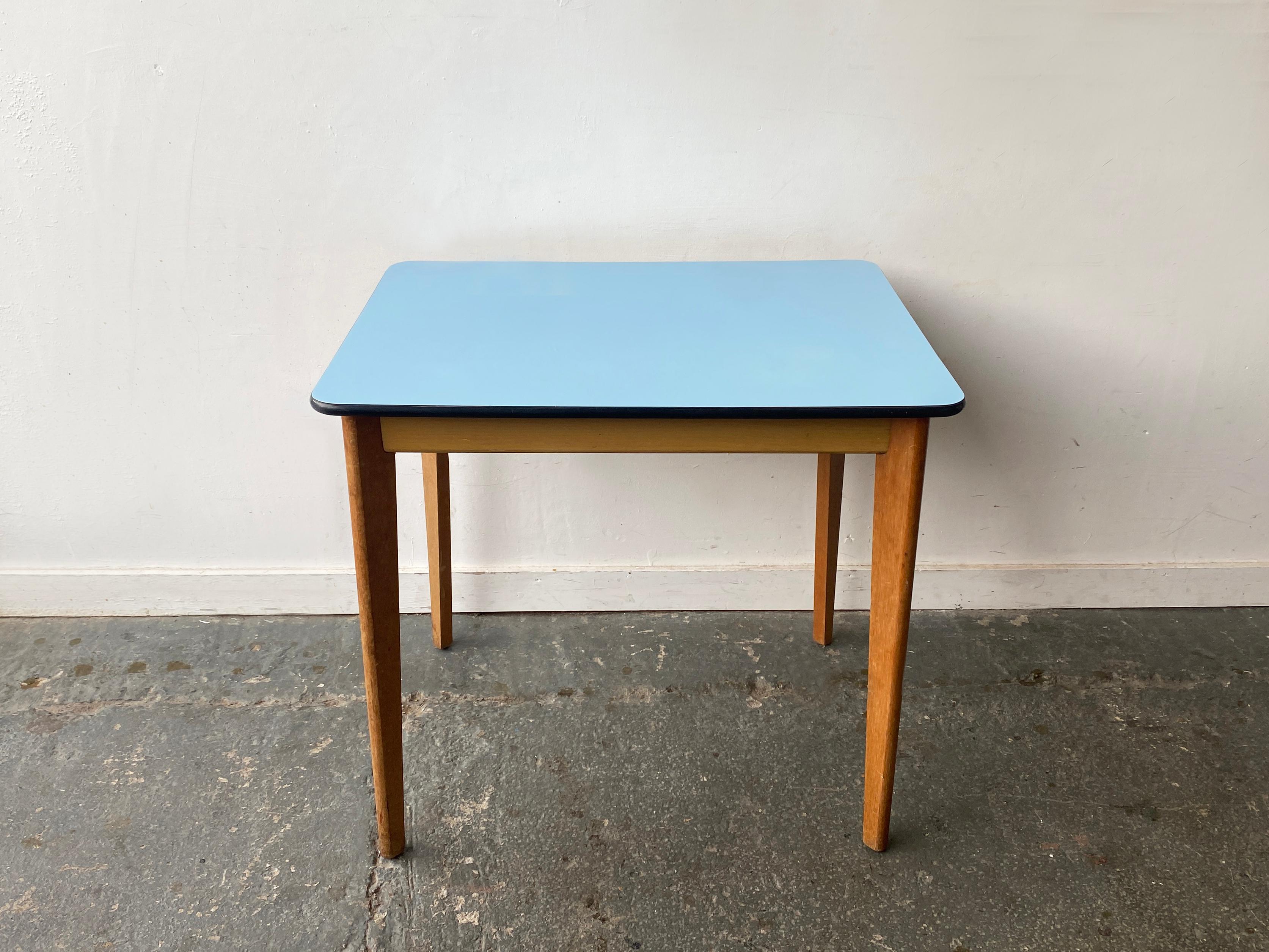 Si tratta di un tavolo da pranzo o da cucina compatto del Mid-Century con piano rettangolare e angoli arrotondati. Il piano del tavolo ha una superficie in Formica laminata blu cielo con una fascia nera sul bordo. Si regge su quattro gambe in