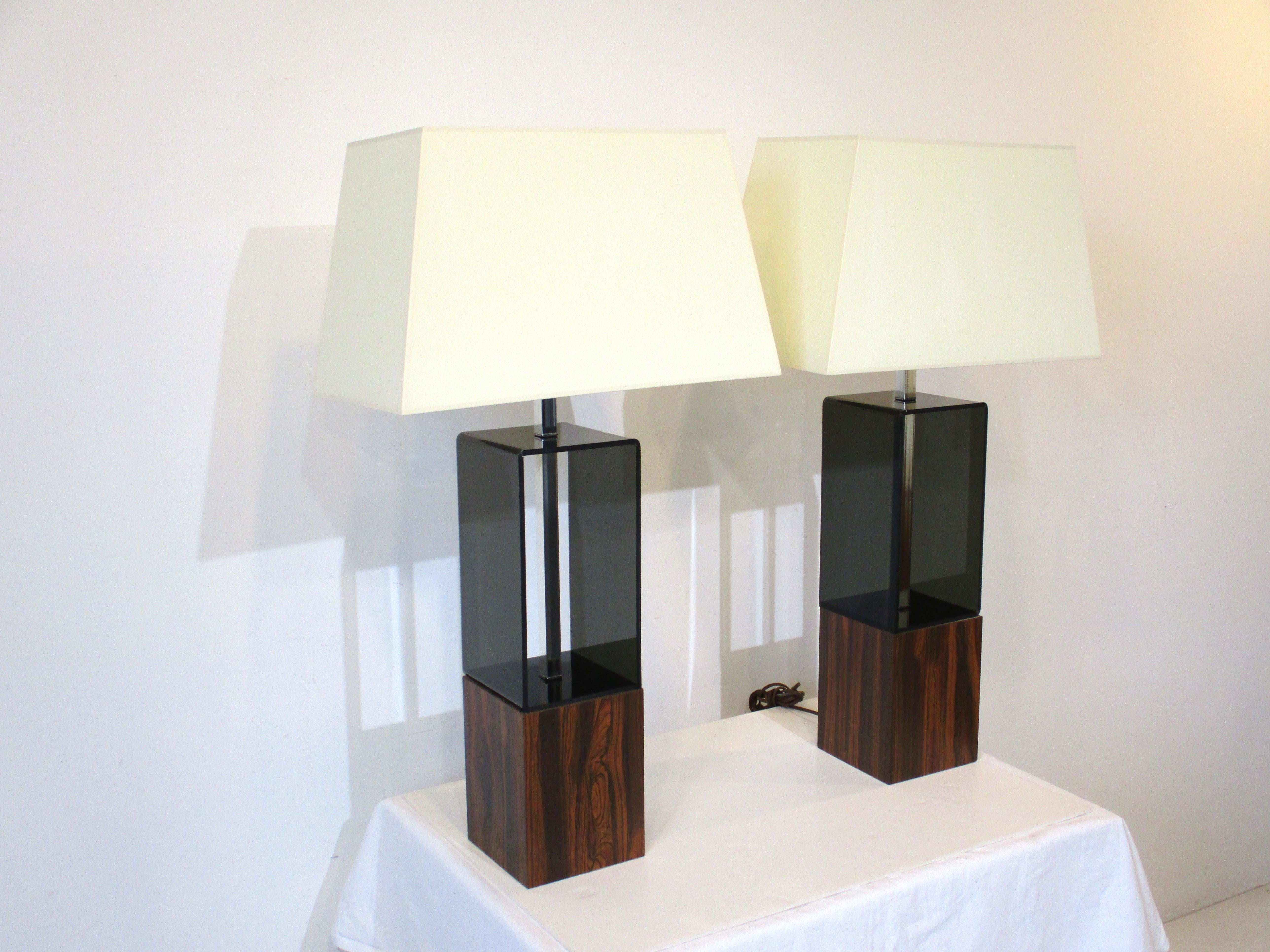 A pair of smoked Lucite and aluminum table lamps with faux rosewood bases which look like the real wood a great pair for overseas importation since rosewood can't be imported to many countries . A nice design for the 1970's . 