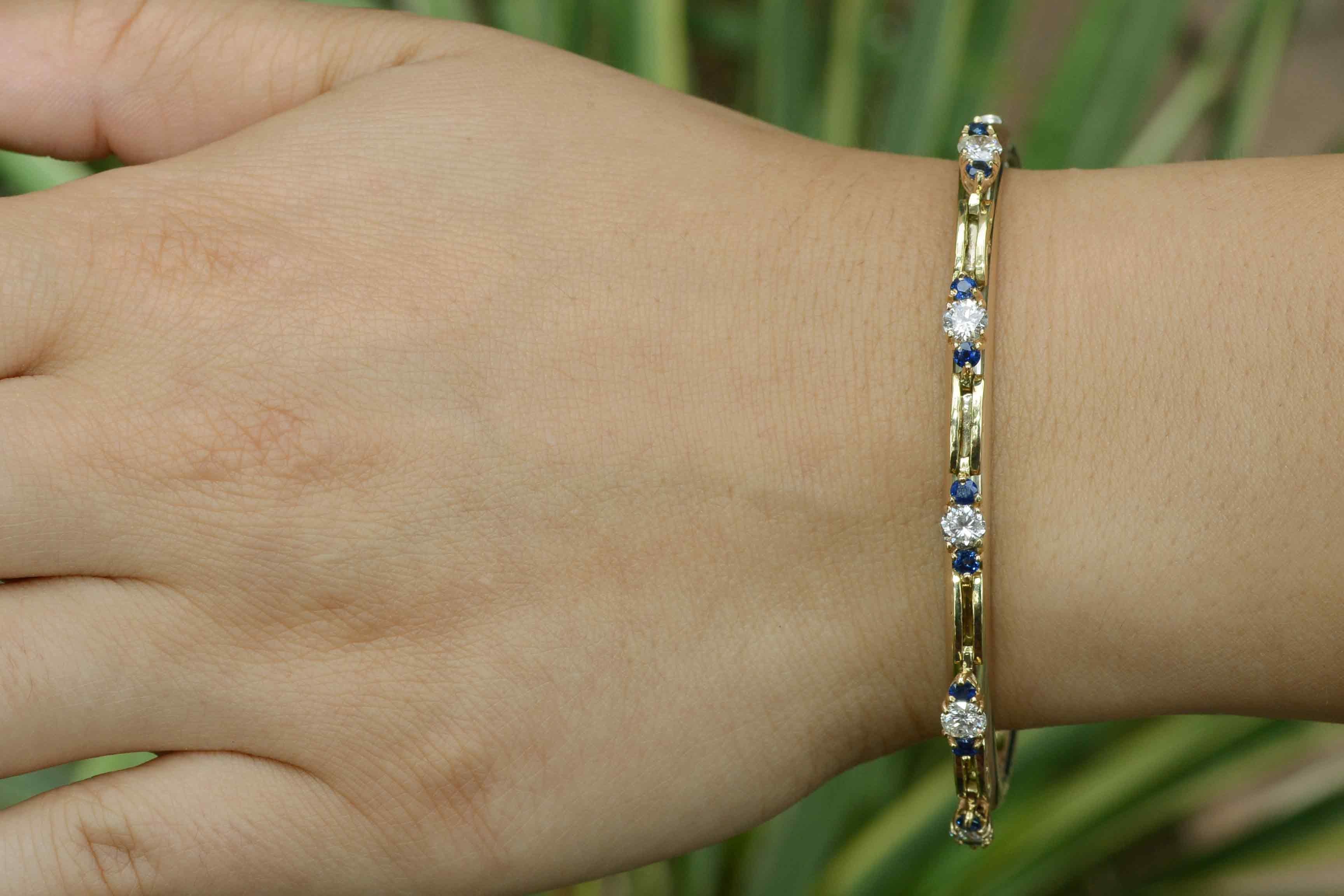 A charismatic, captivating Mid Century sapphire and diamond bangle bracelet that makes a bold statement. 5 brilliant, dazzling round diamonds totaling 1.15 carats are each shouldered by luxurious blue sapphires in a 3 stone pattern. Worn alone or