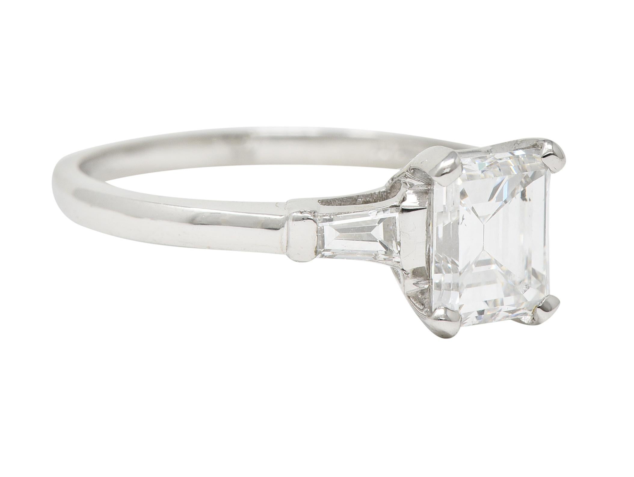 Centering an emerald cut diamond weighing 1.78 carats total - E color with SI1 clarity. Prong set in a basket and flanked by tapered baguette cut diamonds. Weighing approximately 0.24 carat total - well matched to center. Bar set in cathedral style
