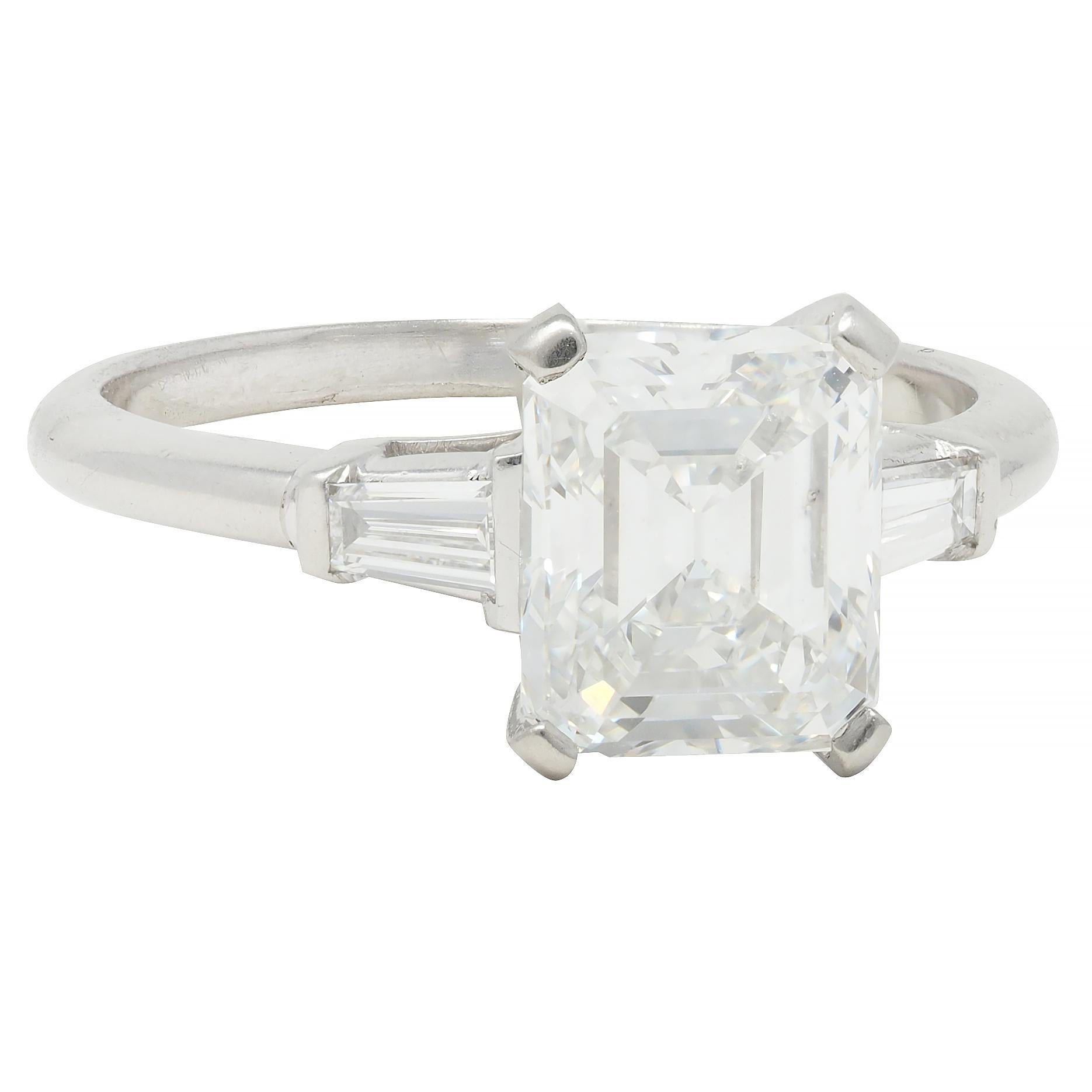 Centering an emerald cut diamond weighing 2.03 carats - F color with VVS2 clarity
Prong set in basket and flanked by tapered baguette cut diamonds 
Weighing approximately 0.14 carat total - well matched to center
Bar set in cathedral