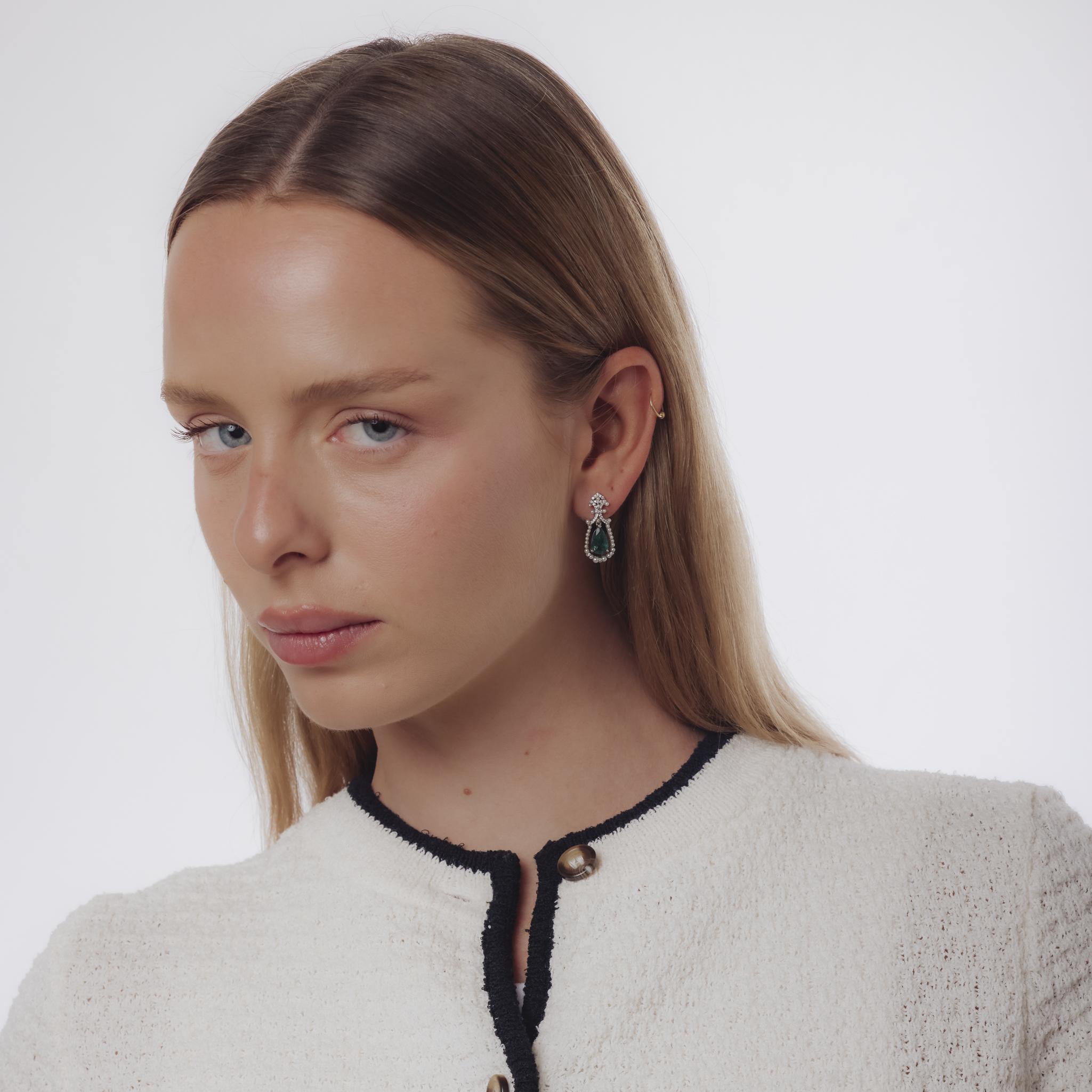Ces boucles d'oreilles du milieu du siècle dernier, datant des années 1950, sont réalisées en or blanc 18 carats et serties de deux émeraudes taille poire totalisant environ 2,35 carats. Les émeraudes sont entourées de soixante-douze diamants ronds