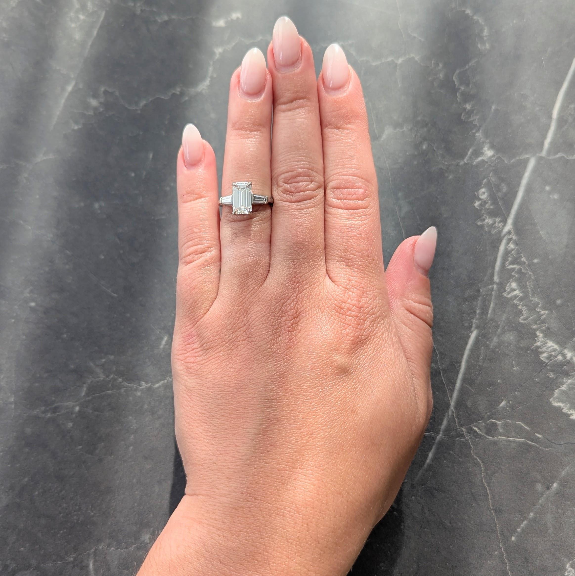Centering an emerald cut diamond weighing 2.20 carats - H color with VS1 clarity
Prong set in basket and flanked by tapered baguette cut diamonds
Weighing approximately 0.36 carat total - well matched to center
Bar set in cathedral shoulders
Stamped
