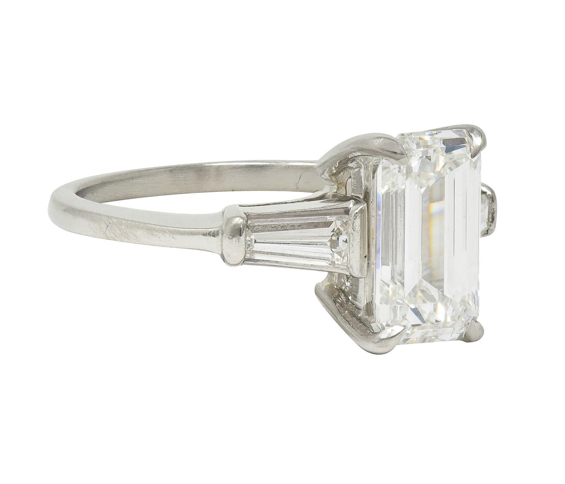 Centering an emerald cut diamond weighing 2.20 carats - H color with VS1 clarity
Prong set in basket and flanked by tapered baguette cut diamonds
Weighing approximately 0.36 carat total - well matched to center
Bar set in cathedral shoulders