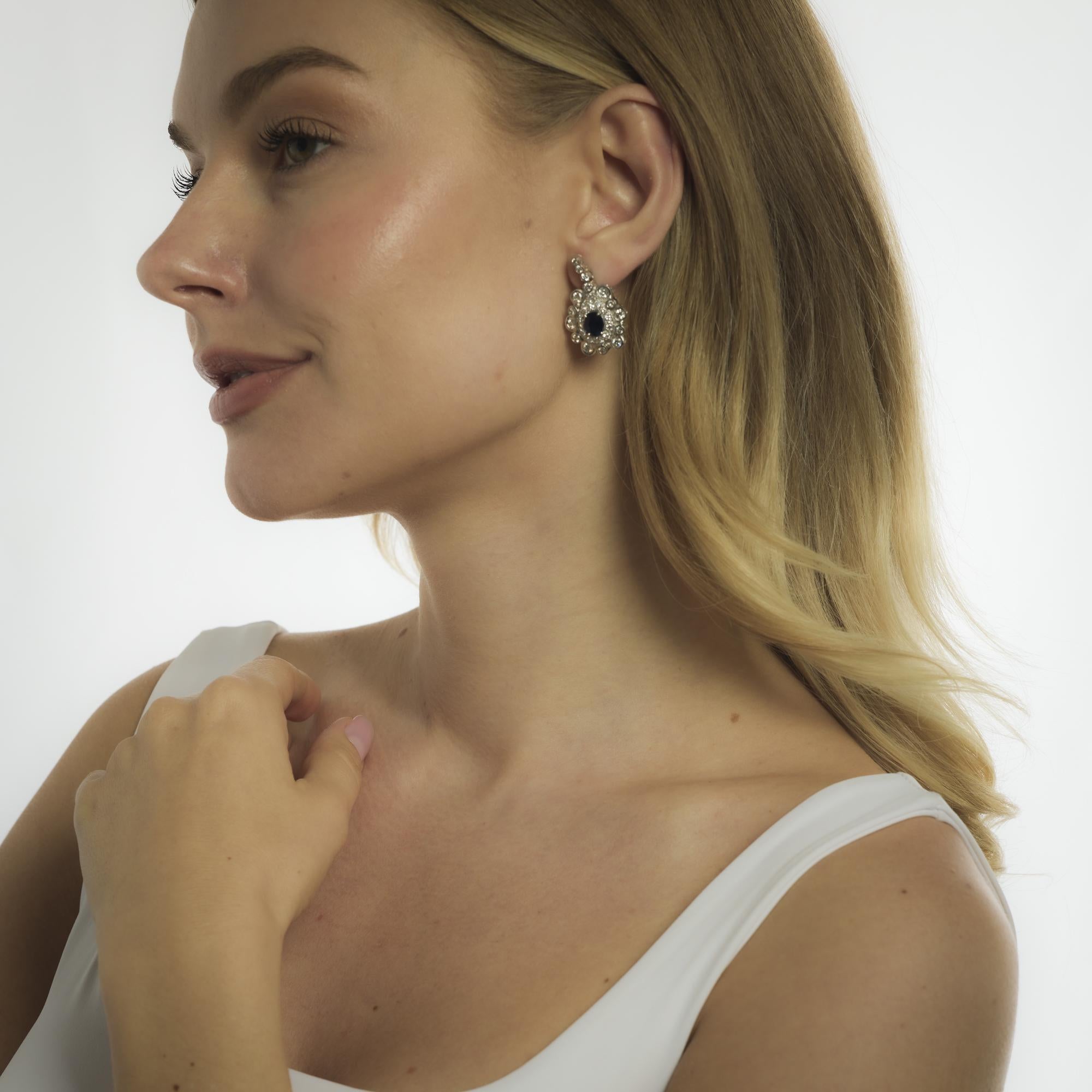 These mid-century earrings from the 1950’s feature two oval cut blue sapphires totaling approximately 2.80 carats, their deep hue framed by fifty-six round brilliant cut diamonds totaling approximately 3.00 carats in H color and SI clarity. Crafted