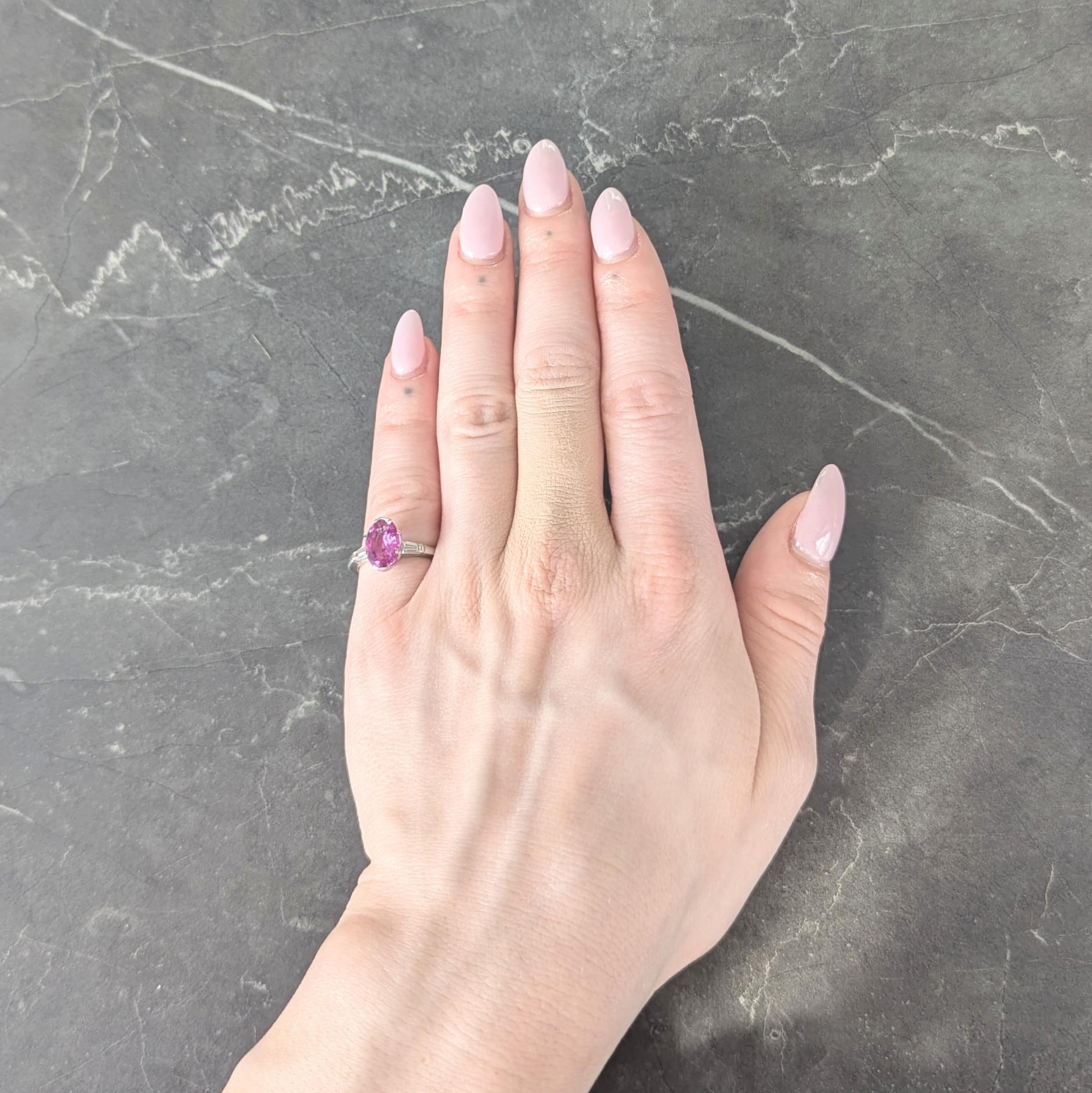 Centering an oval cut sapphire weighing 2.53 carats - transparent medium purple-pink in color
Natural and displaying no indications of heat treatment - prong and bar set in a pierced basket
Flanked by cathedral shoulders bar set with tapered