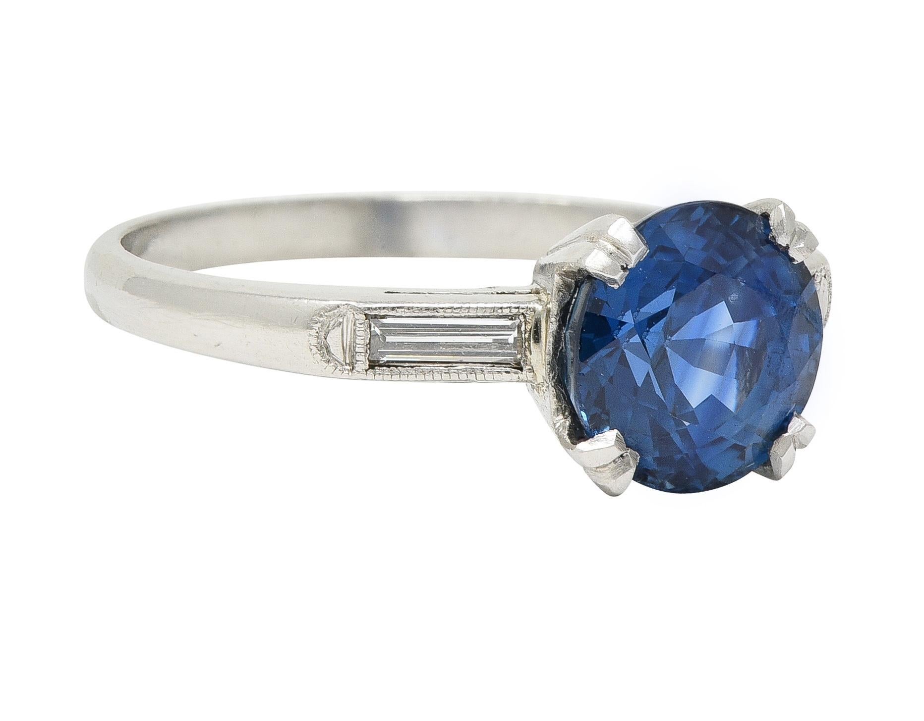 Centering a round cut sapphire weighing 2.80 carats - transparent medium-dark blue
Natural Thai in origin with no indications of heat treatment 
Set with split prongs in a pierced foliate motif basket
Flanked by cathedral shoulders bezel set with