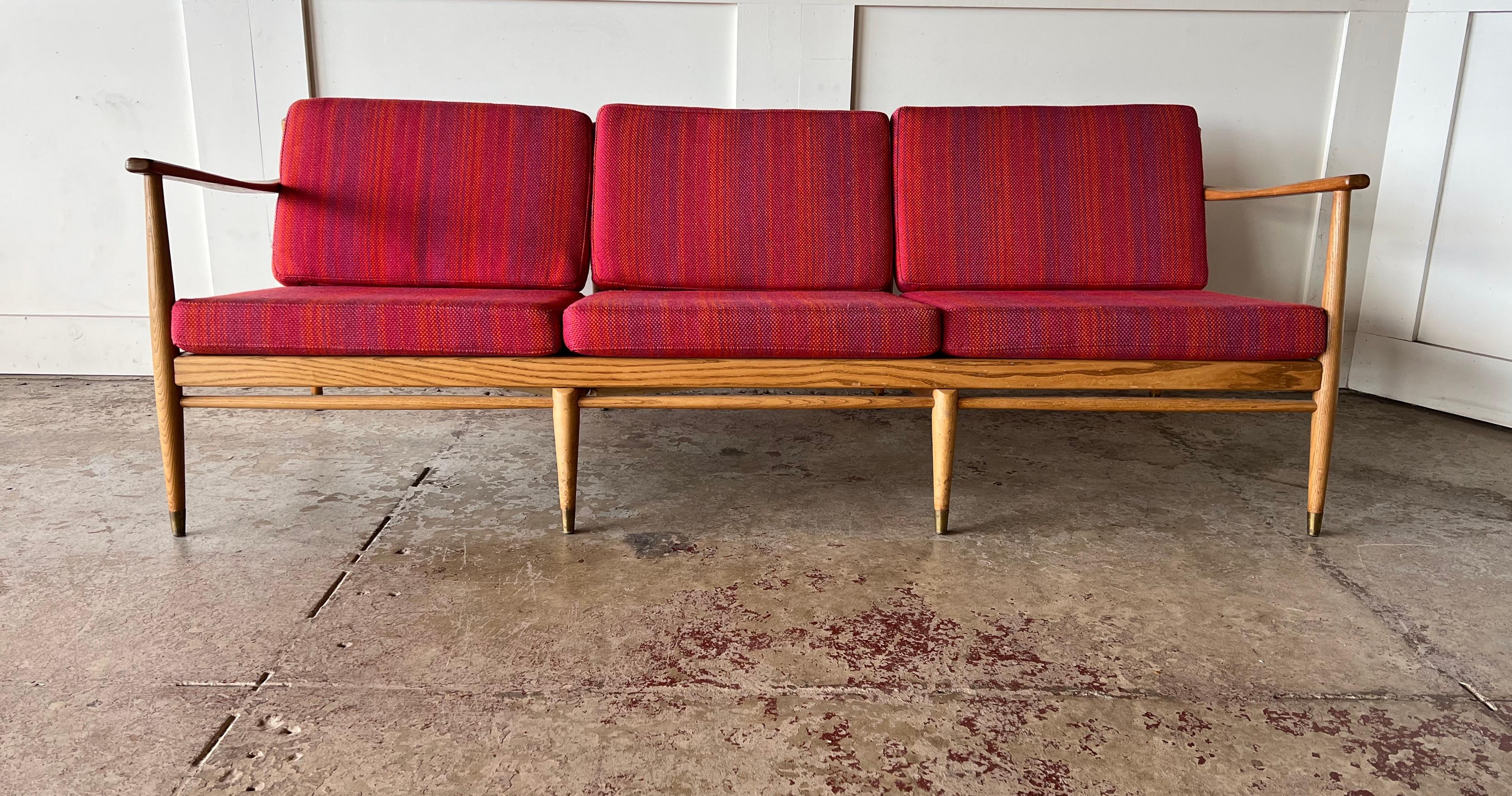 This three-seat sofa is a mid-century Danish design, inspired by the iconic style of Hans J. Wegner. The sofa features a cigar shape to the armrests and is upholstered in its original wool fabric. It is accented with a contrasting wide striped