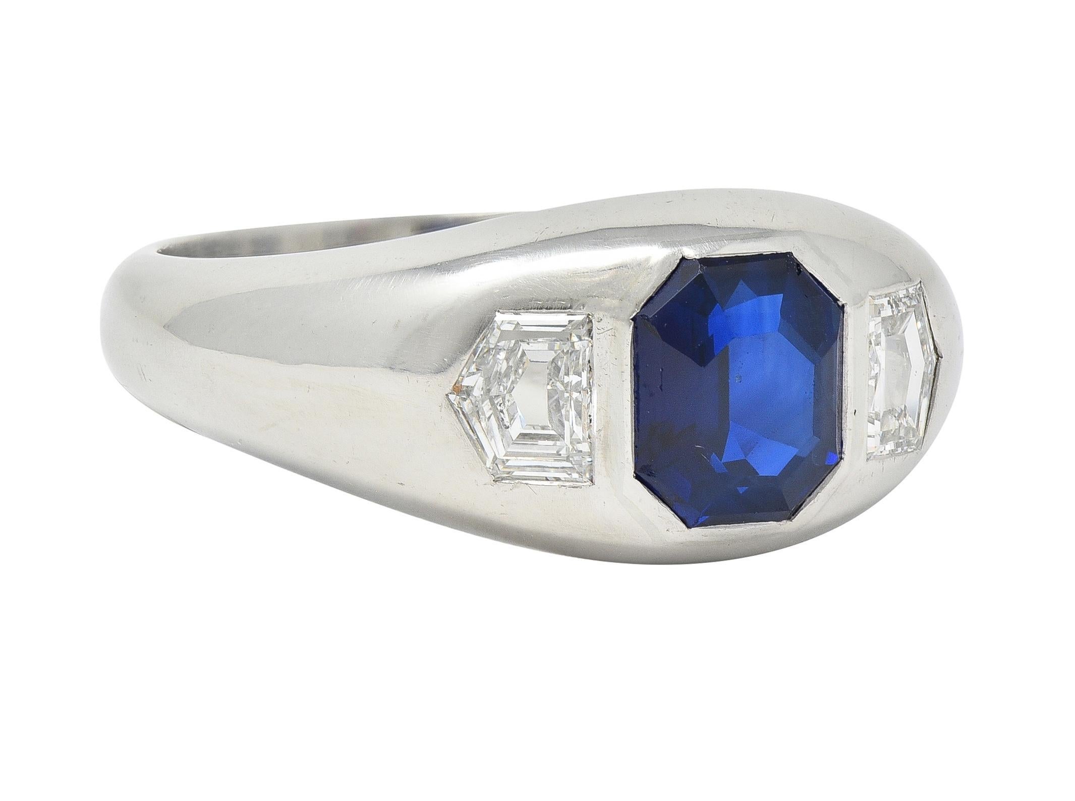 Centering an octagonal step-cut sapphire weighing 2.33 carats - transparent dark blue 
Natural Cambodian in origin with no indications of heat treatment
Flush set and flanked by pentagonal step-cut diamonds 
Weighing approximately 0.74 carat total -