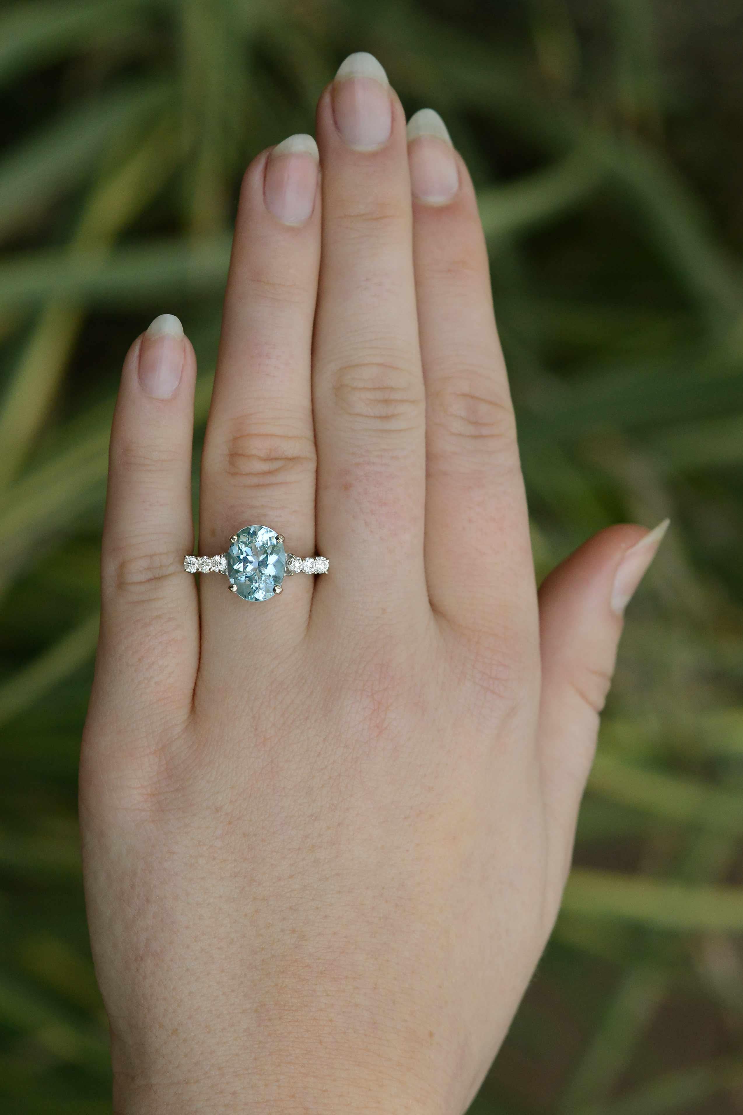 A charming, vintage aquamarine engagement ring displaying deep saturation and a vivid ocean blue color. The oval faceted oceanic gemstone is 3.20 carats total with great clarity. 6 round brilliant diamonds are prong set into the graceful 18k white