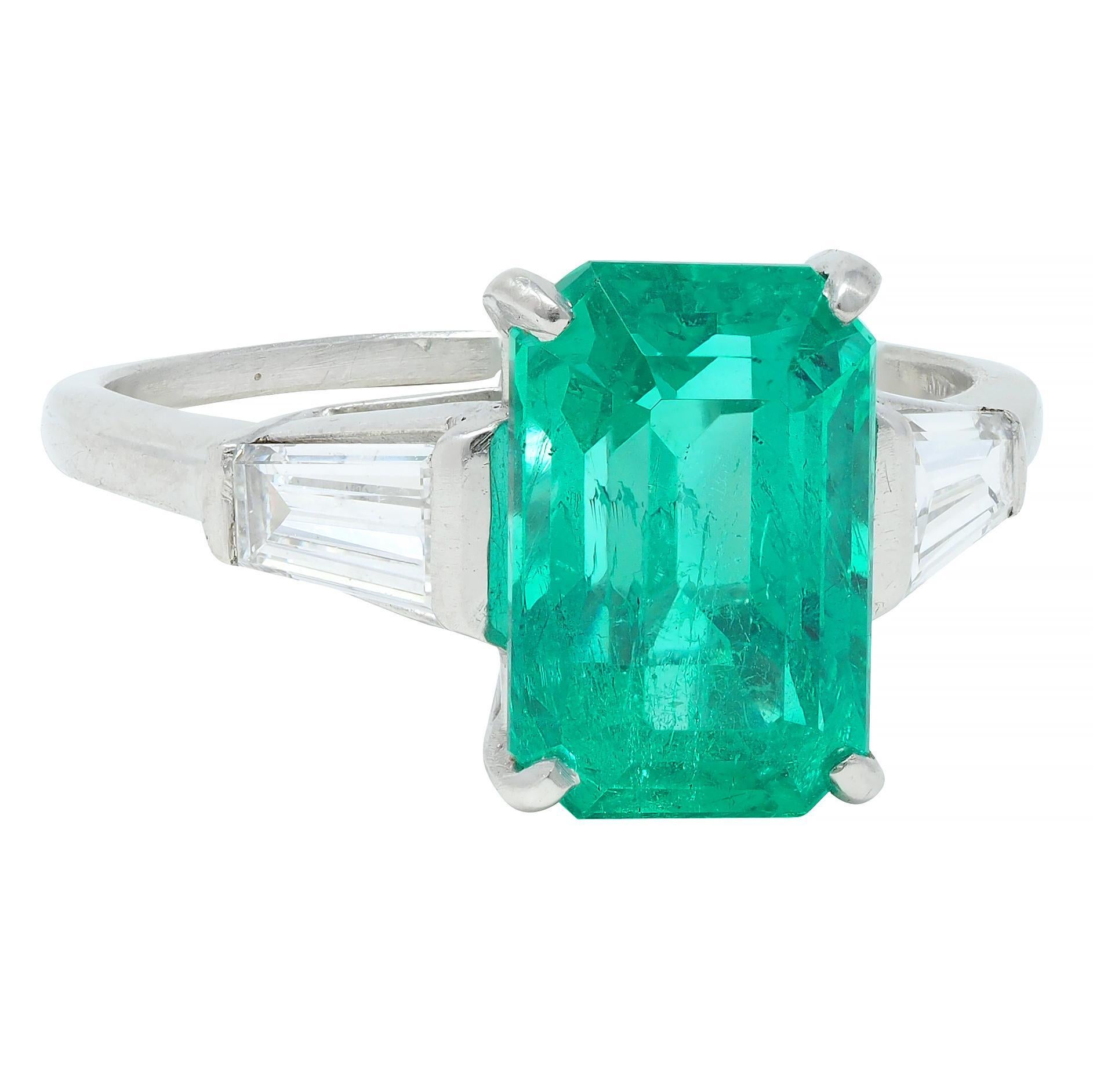 Centering an emerald cut emerald weighing 2.93 carats total - transparent medium green
Natural Colombian in origin and displaying minor traditional clarity enhancement 
Prong set in basket and flanked by tapered baguette cut diamonds
Weighing