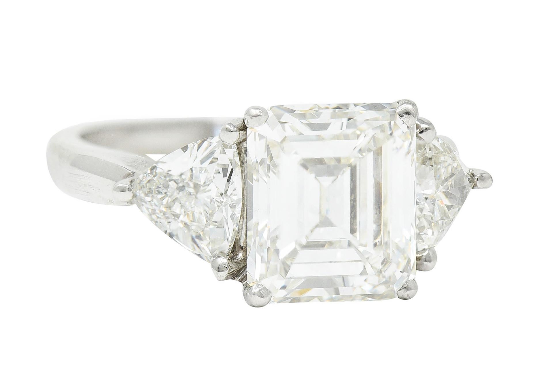 Centering an emerald cut diamond weighing 2.95 carats - J color with VVS2 clarity

Basket set and flanked by cathedral shoulders set with trilliant cut diamonds

Weighing in total approximately 0.75 carat with well matched J color and VS