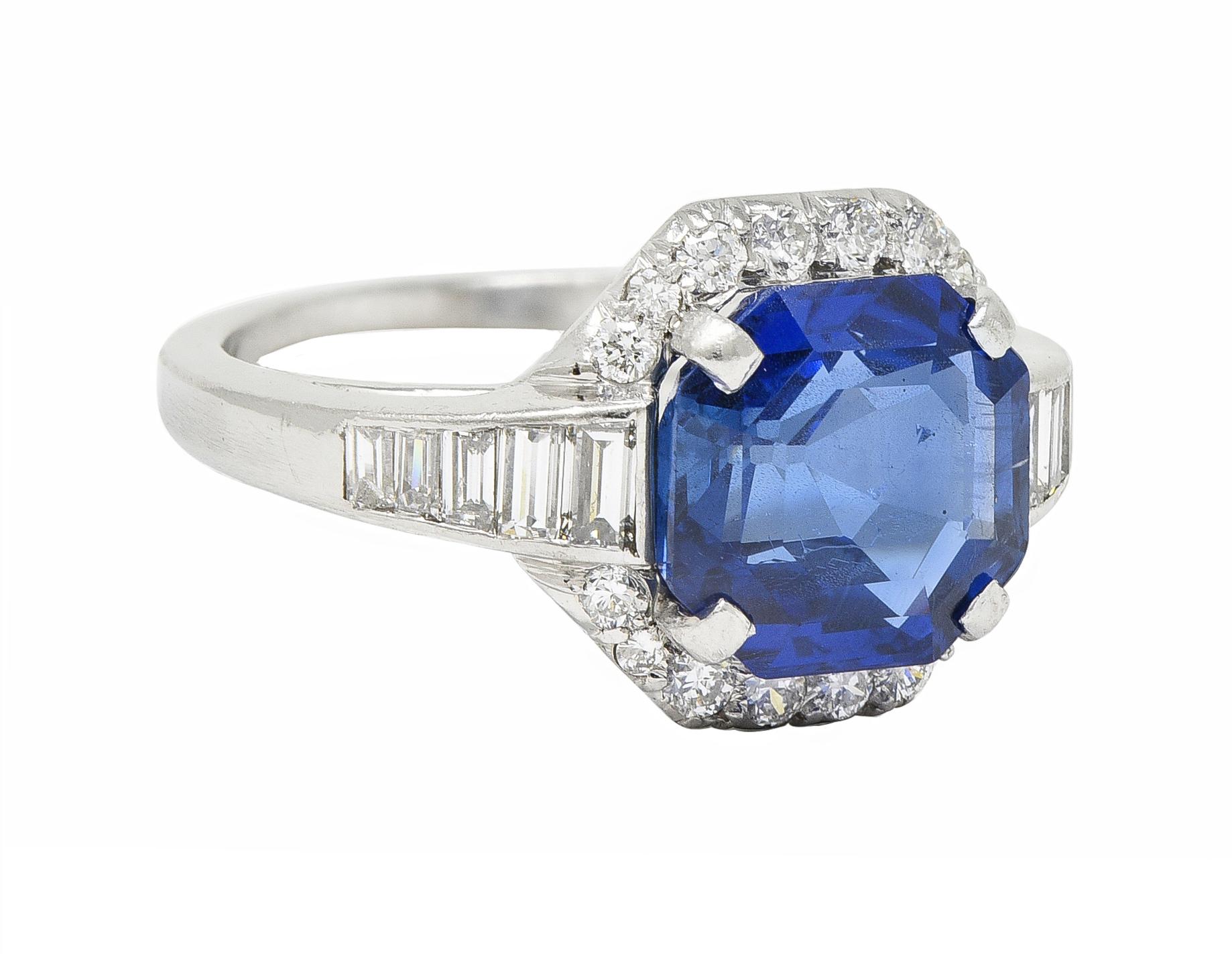 Centering an octagonal step cut sapphire weighing 3.49 carats - transparent medium blue
Natural Burmese in origin with no indications of heat treatment - prong set
With a halo surround of round brilliant cut diamonds 
Bisected by baguette cut